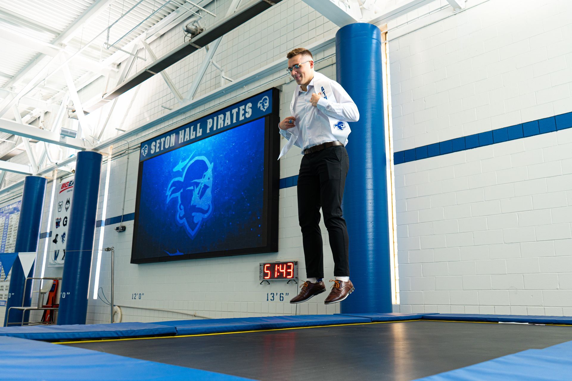 Person standing on a stage beside a screen in a blue and white gymnasium