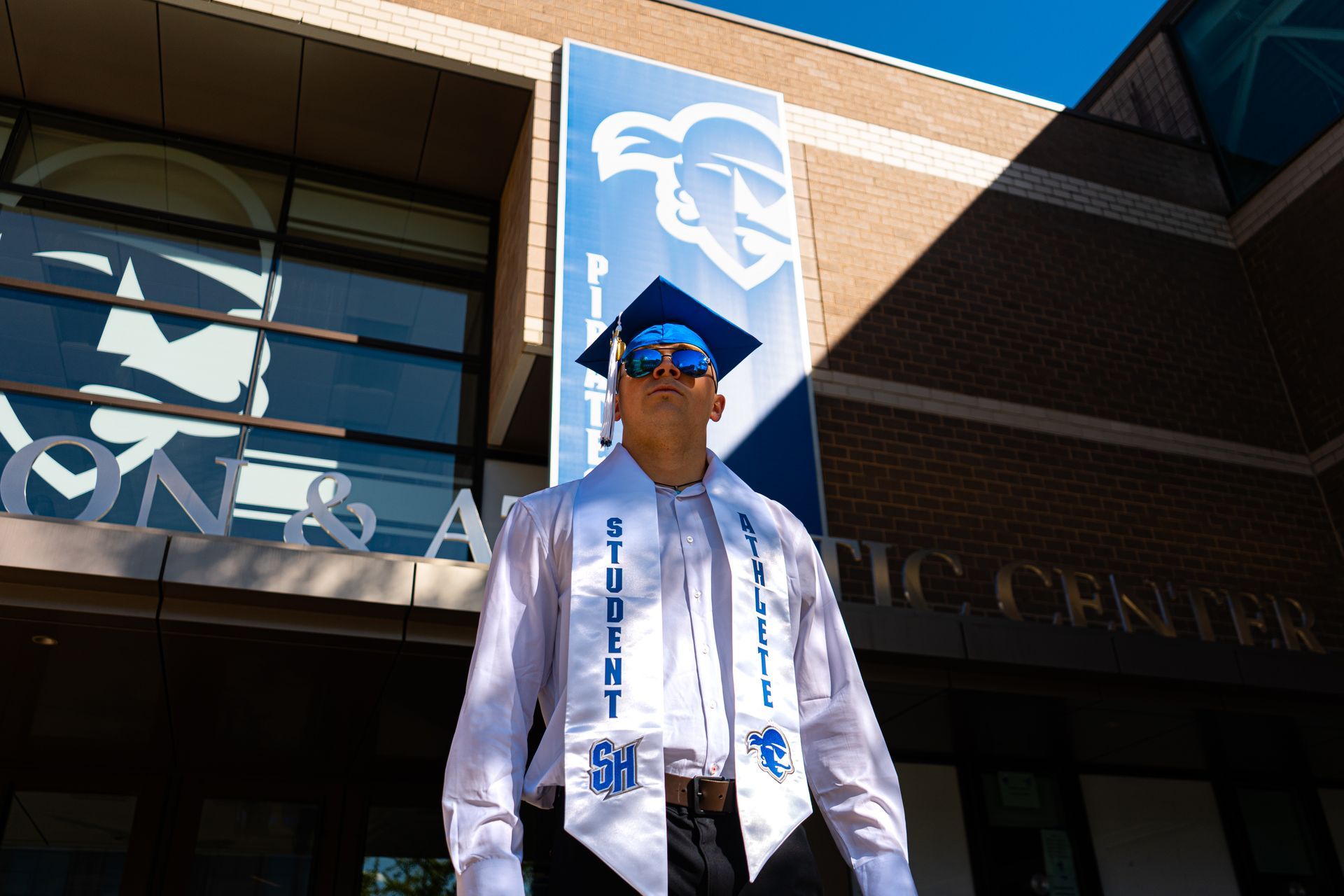 Person in blue cap and white shirt stands outside a building with a large blue sign.