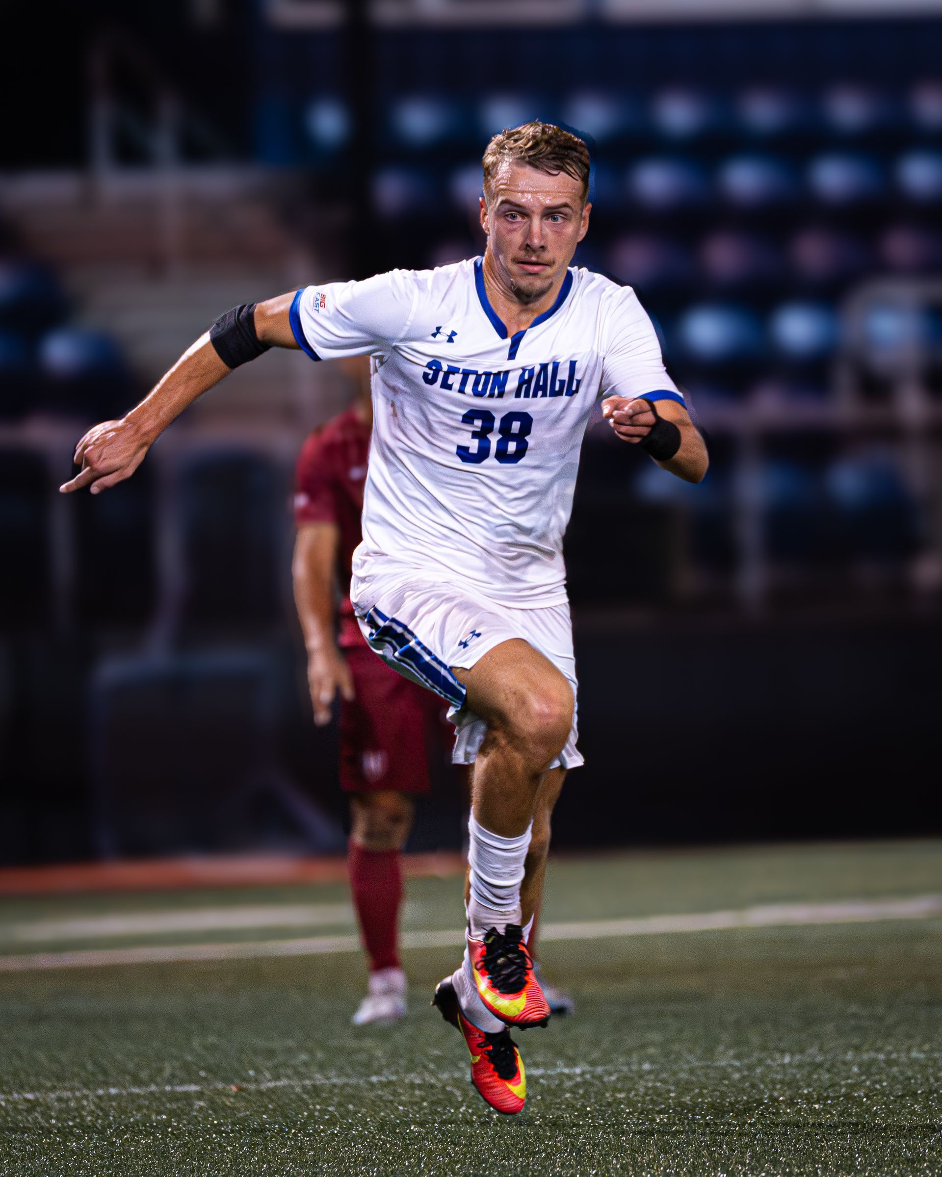 Soccer player in white jersey #38 sprinting on a field at night