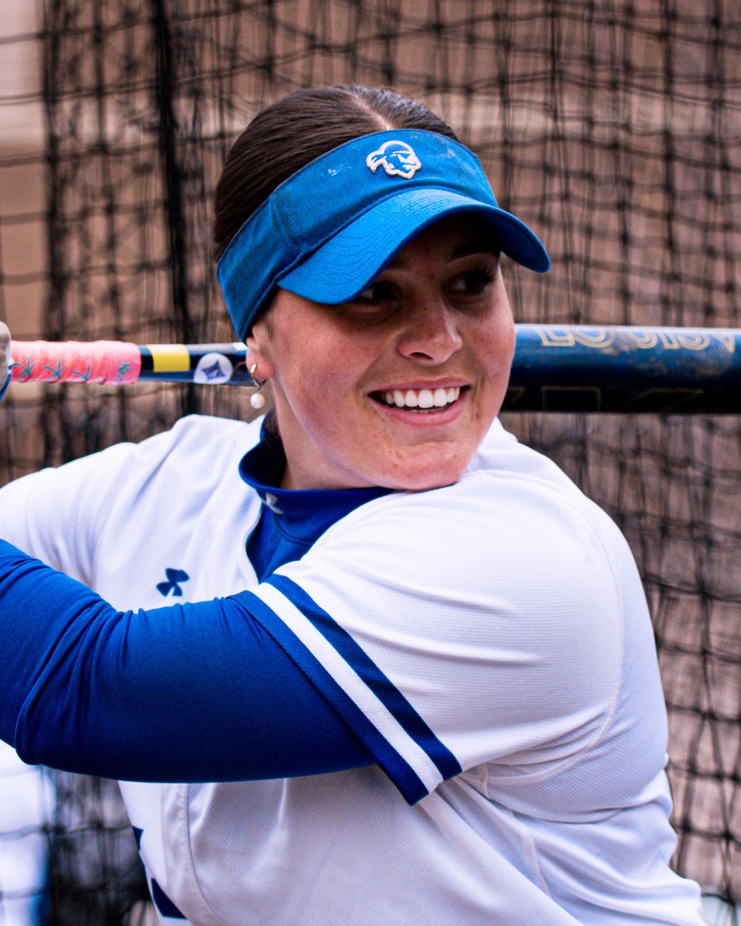 Smiling softball player in blue visor and white jersey holding a bat on the field