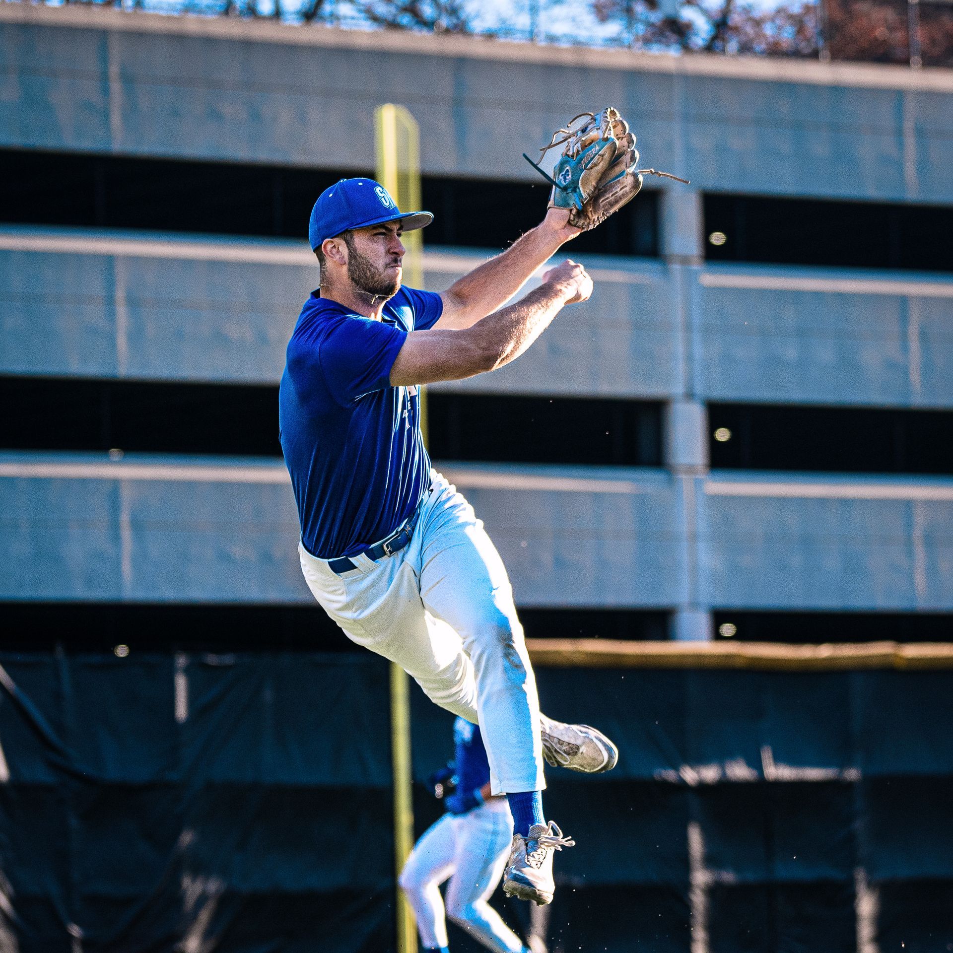 Baseball player in blue jumps to catch a ball in front of a stadium backdrop