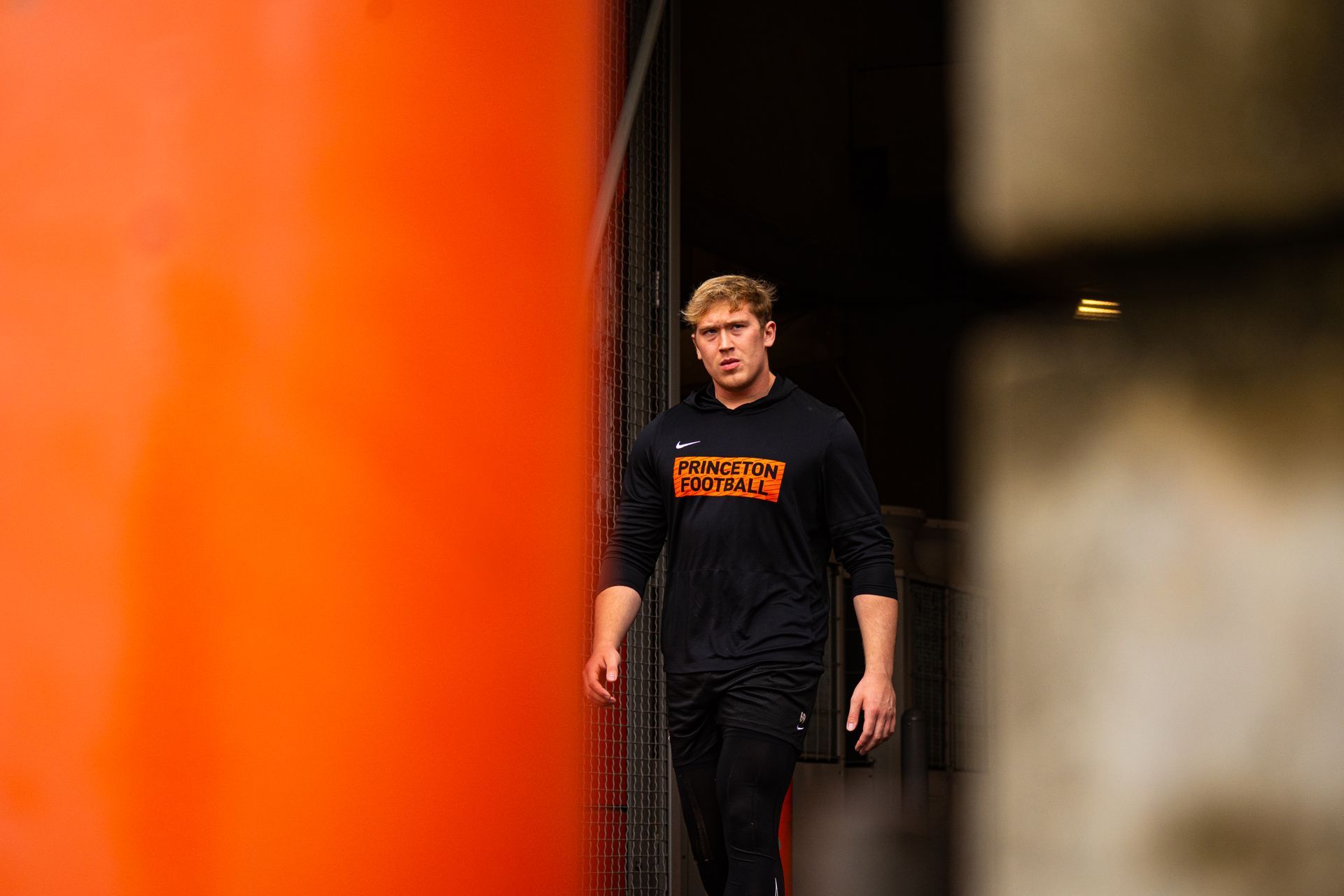 Person in black walking beside a large orange column in a dim indoor space
