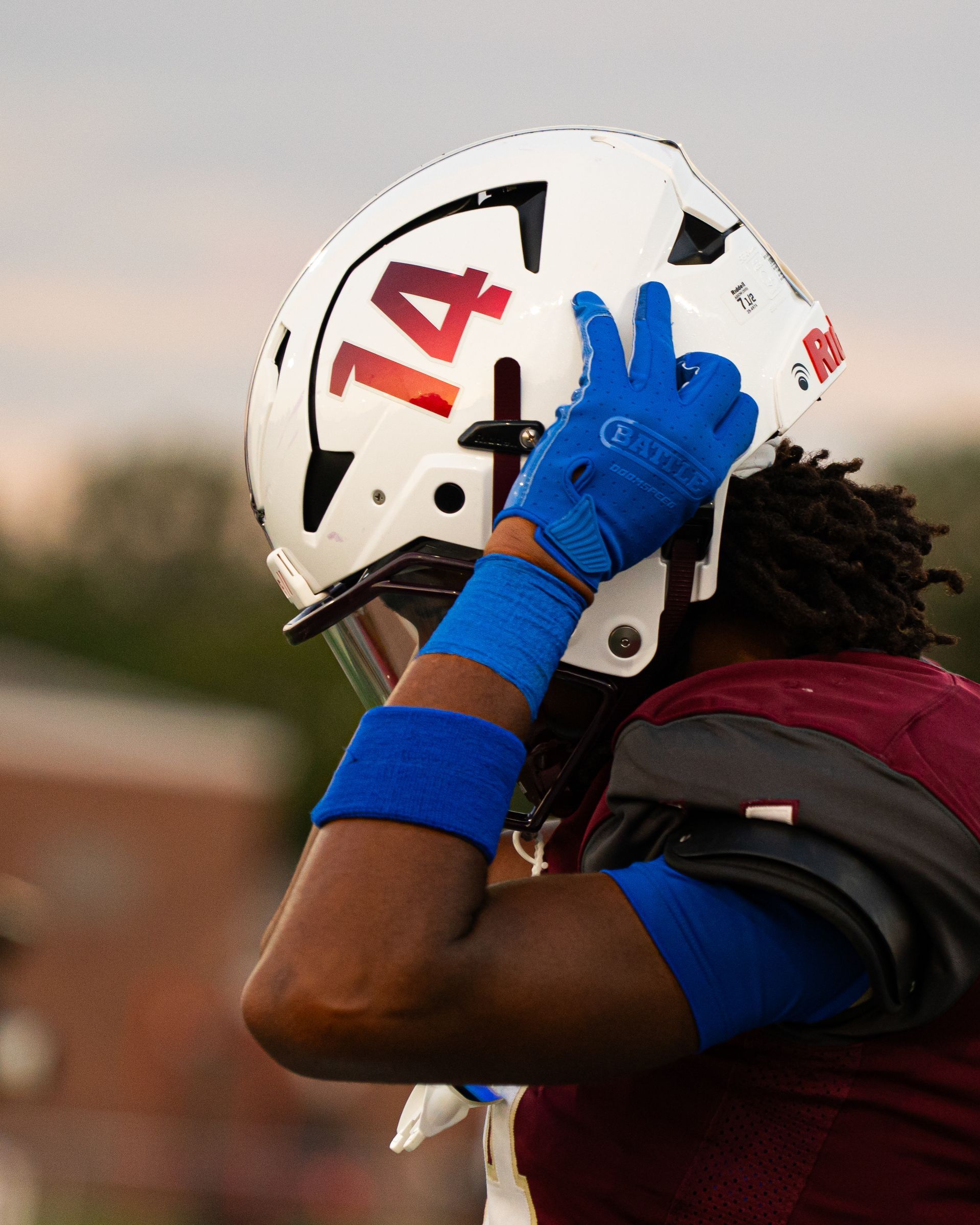 Football player in maroon jersey adjusting a white helmet marked 14