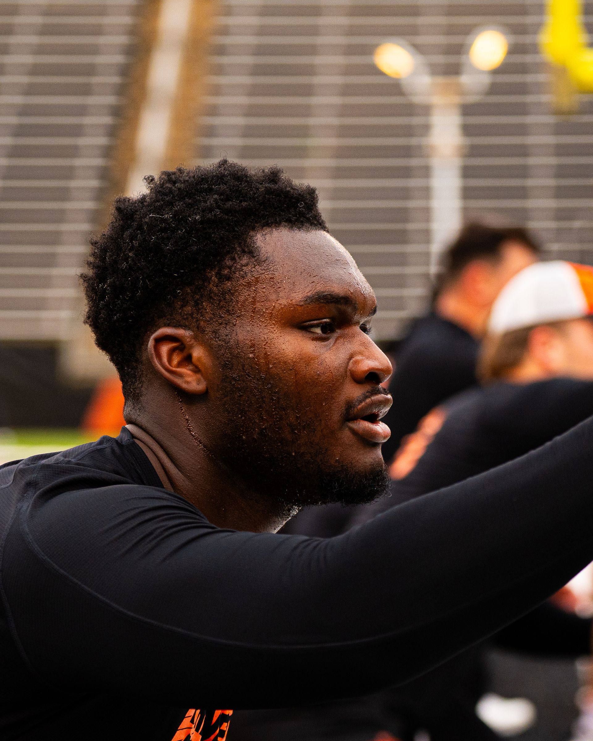 Athlete in black shirt reaching forward indoors, with blurred spectators in the background.