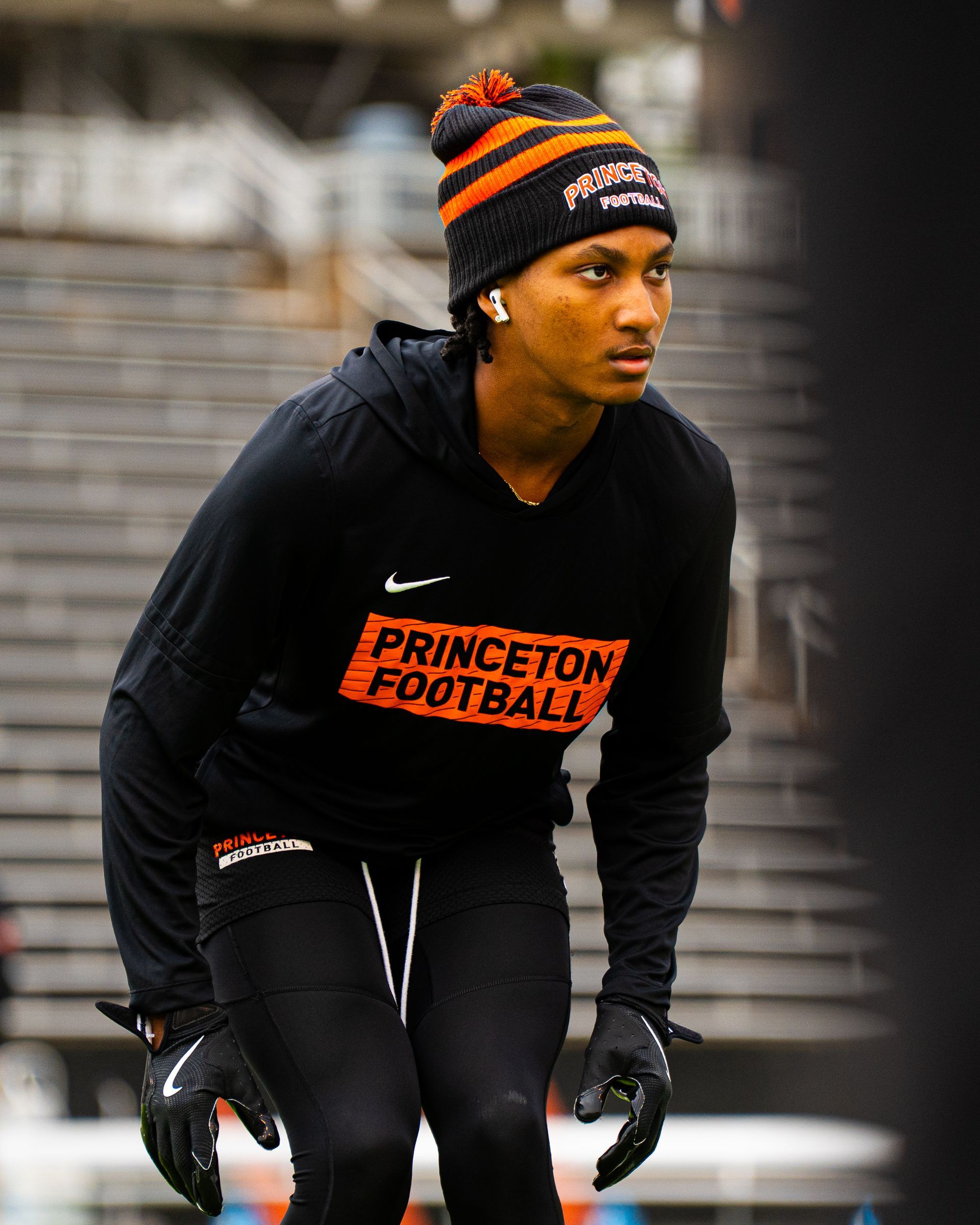 Princeton football player in black warm-up gear and striped beanie, crouched on the field, looking right
