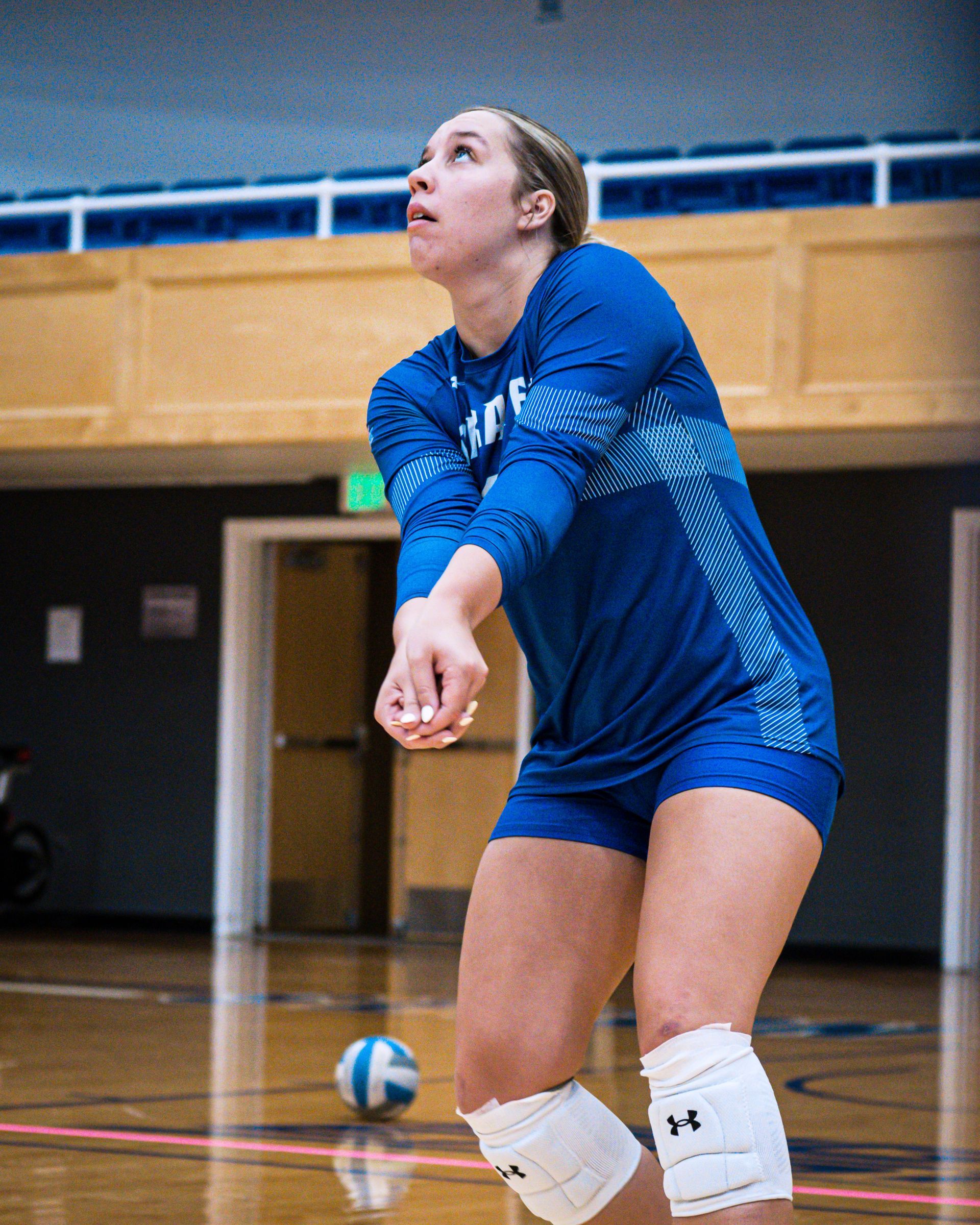 Volleyball player in blue jersey preparing to serve on an indoor court