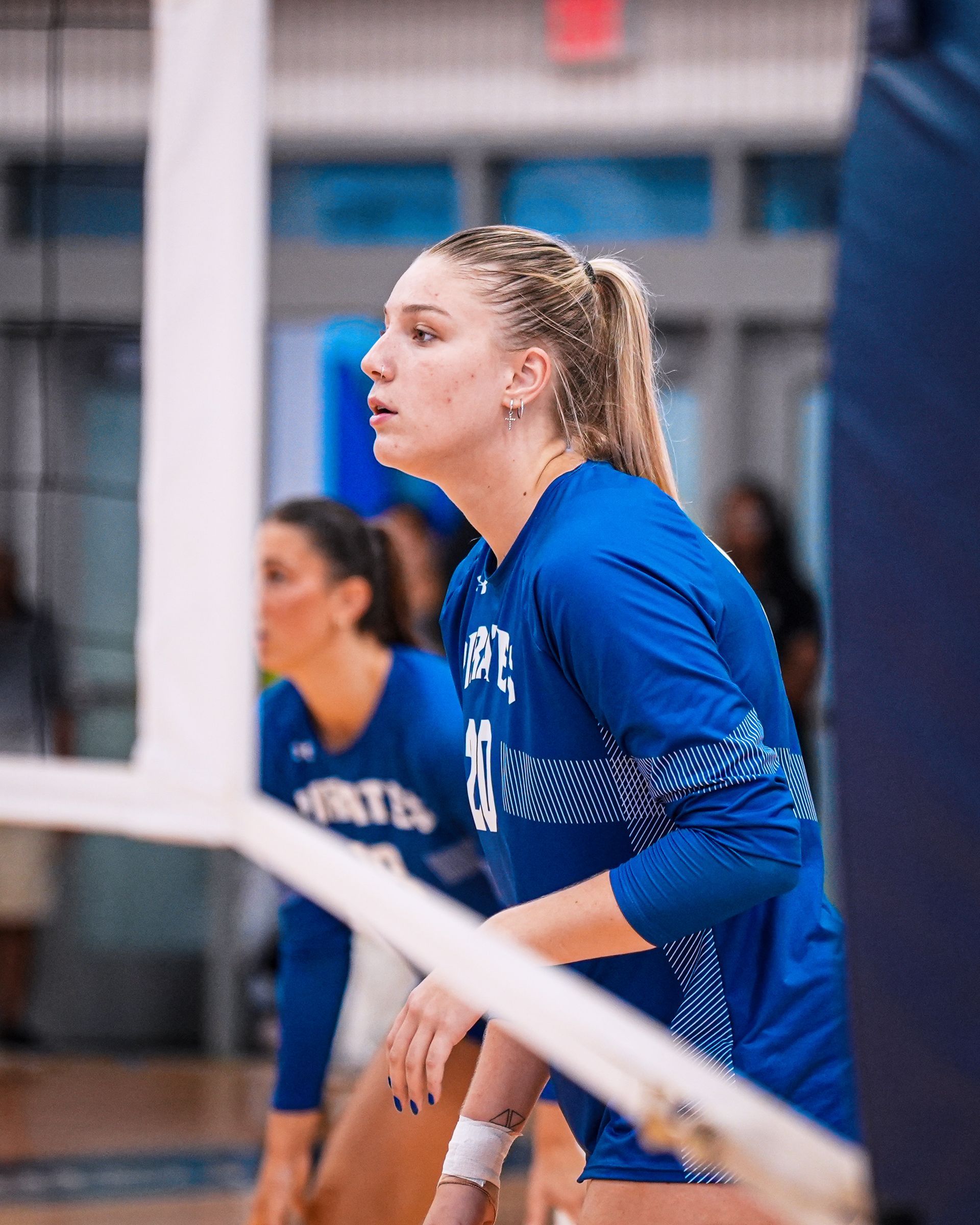 Volleyball player in blue jersey crouches near the net during an indoor match