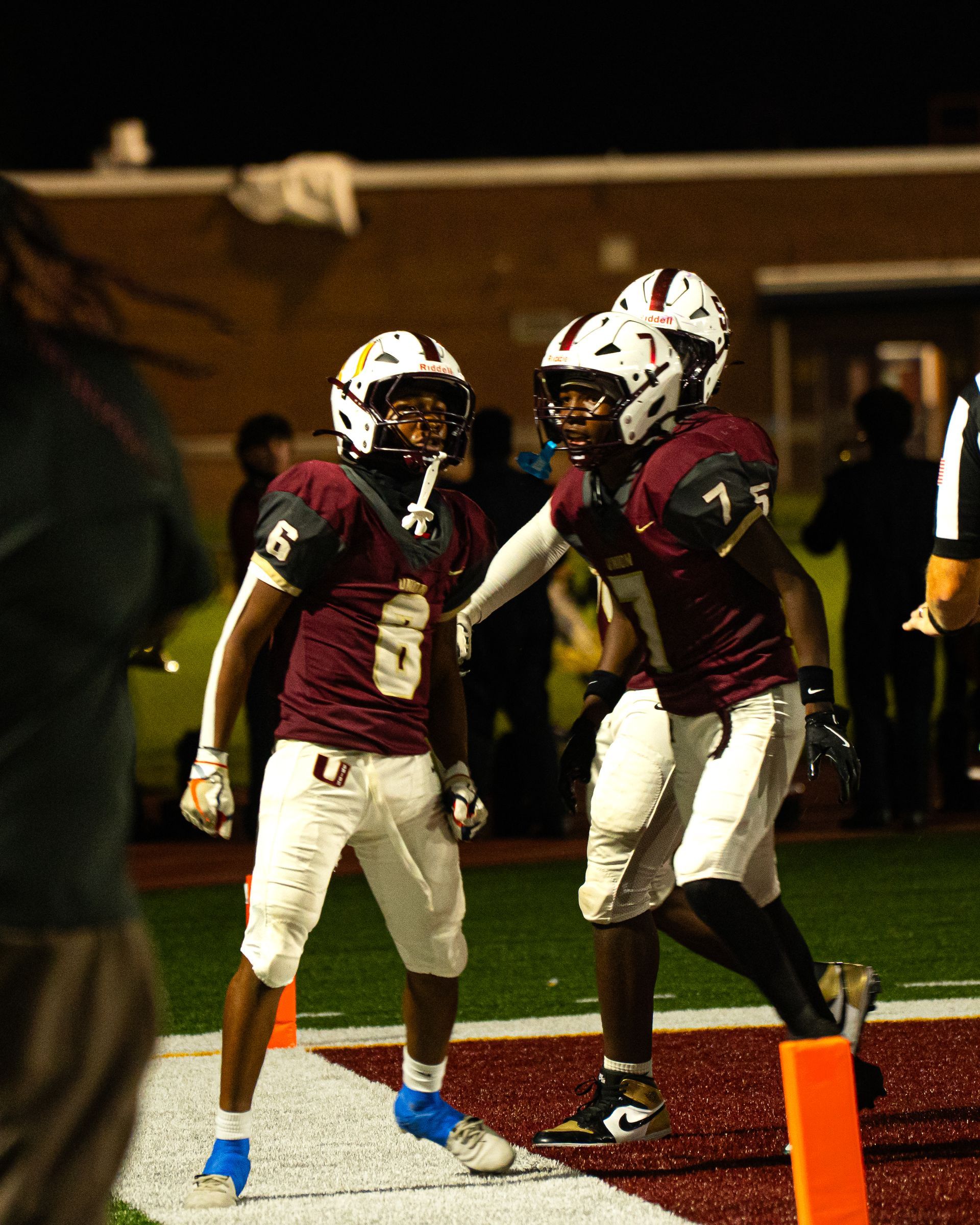 Two football players in maroon uniforms celebrating in the end zone at night