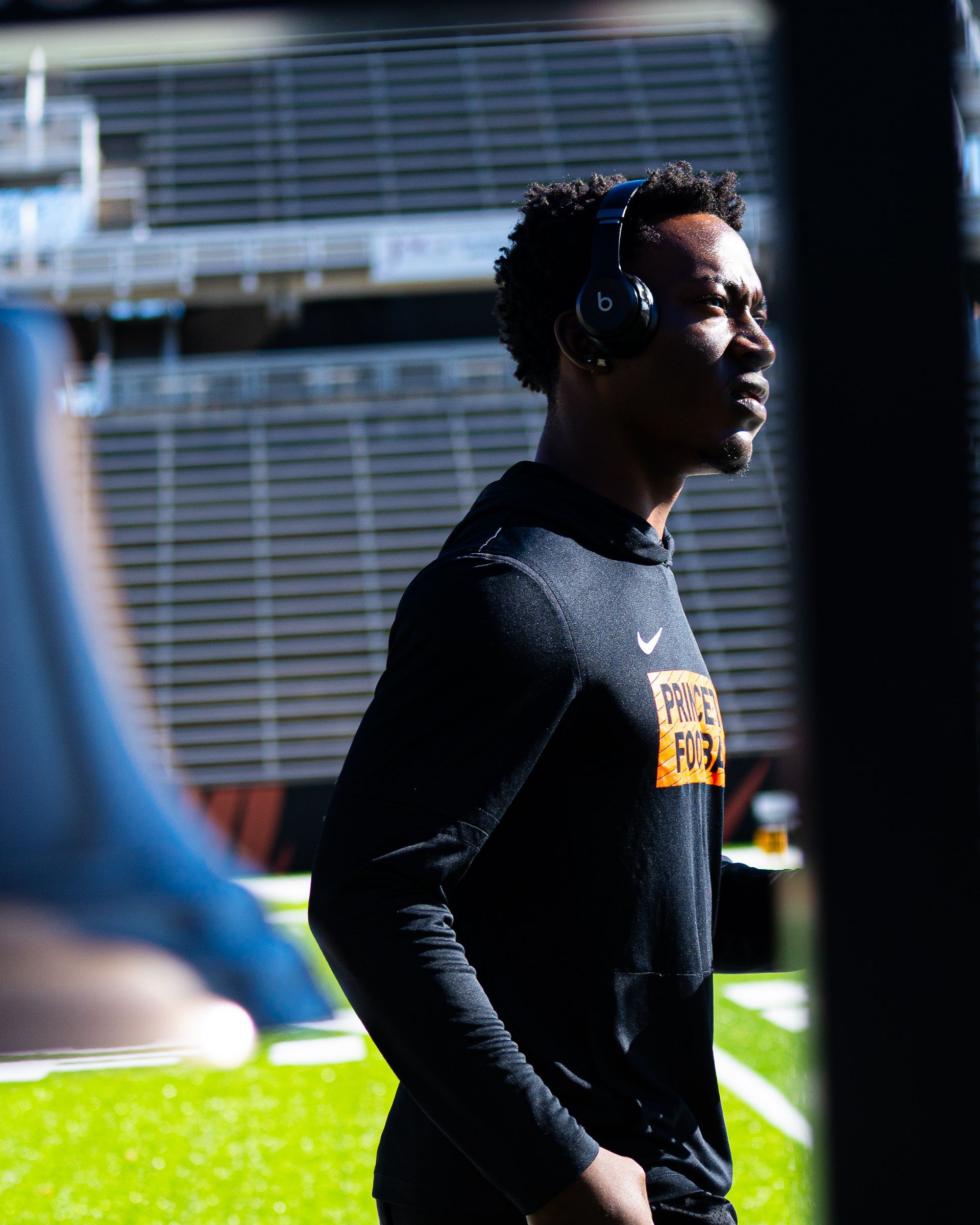 Athlete in black long-sleeve shirt standing on a track field in sunlight.