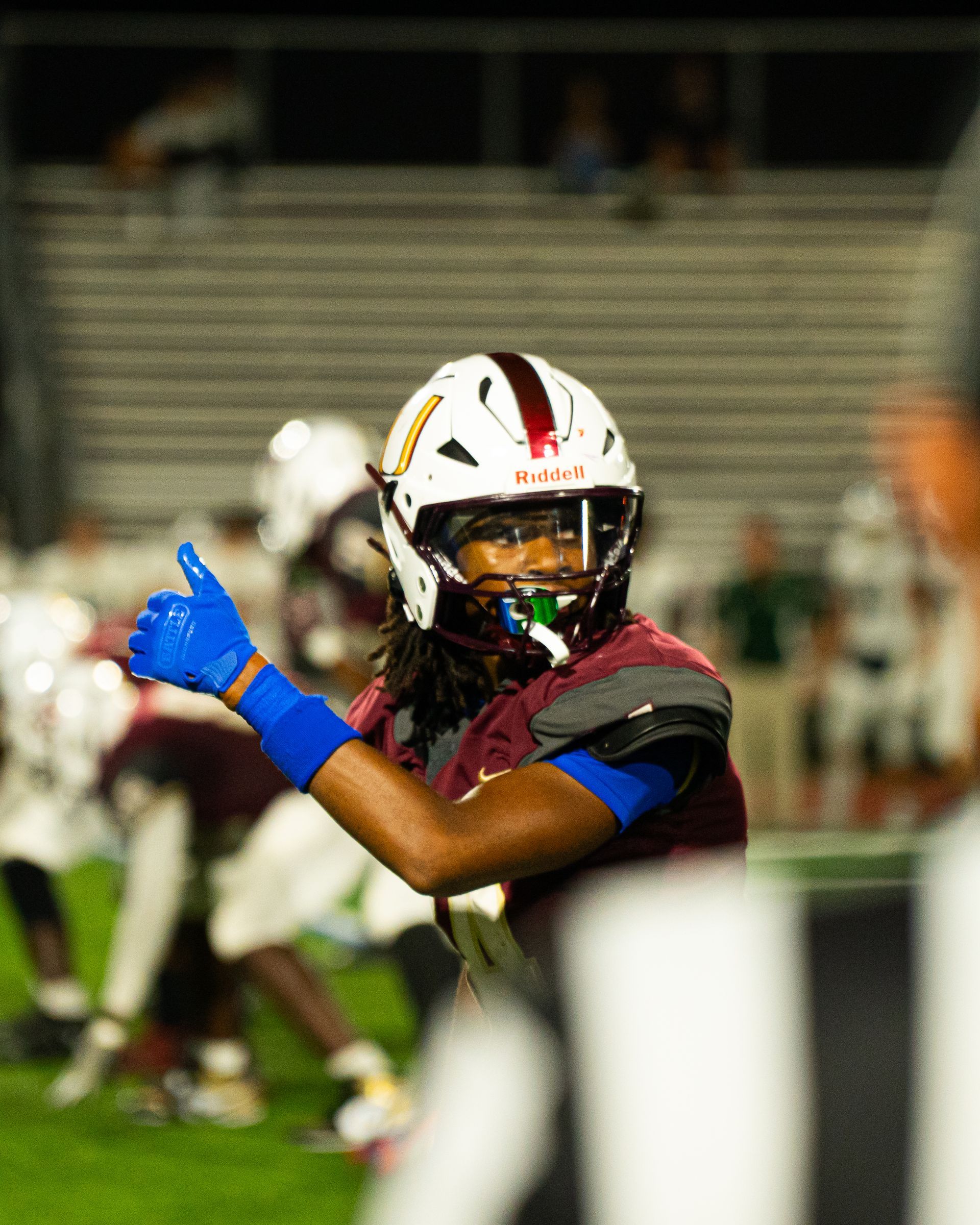Football player in white helmet and blue glove preparing to throw on the field at night