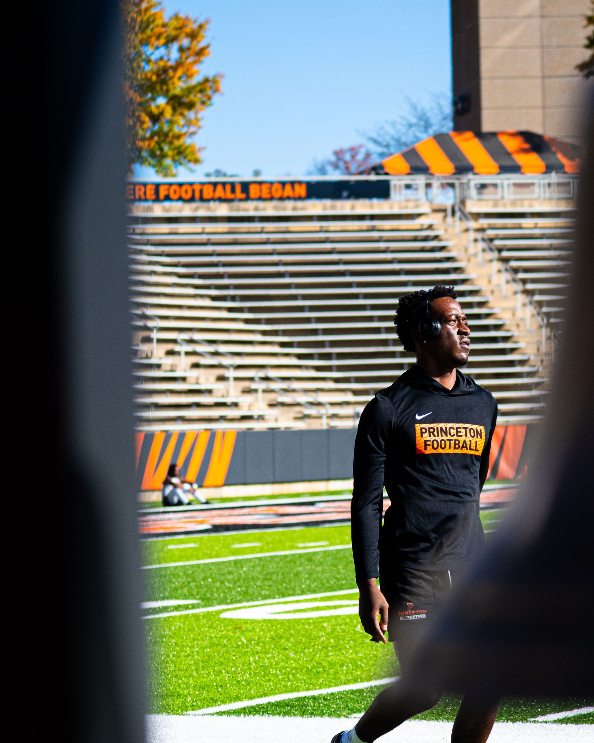 Football player in black standing on a stadium field with bleachers in the background