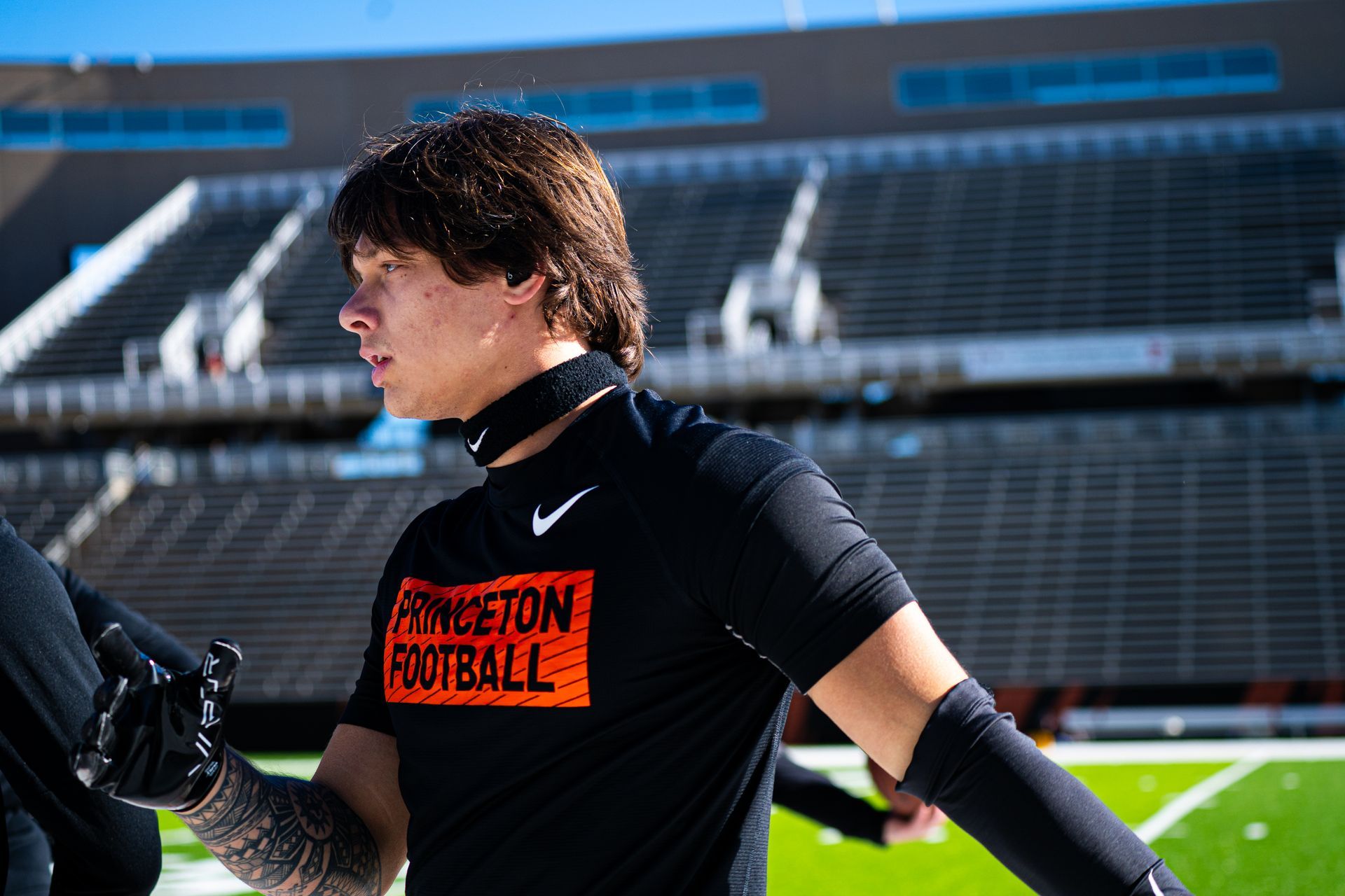 Soccer player in black shirt and gloves stands on a field in a stadium, looking to the side.