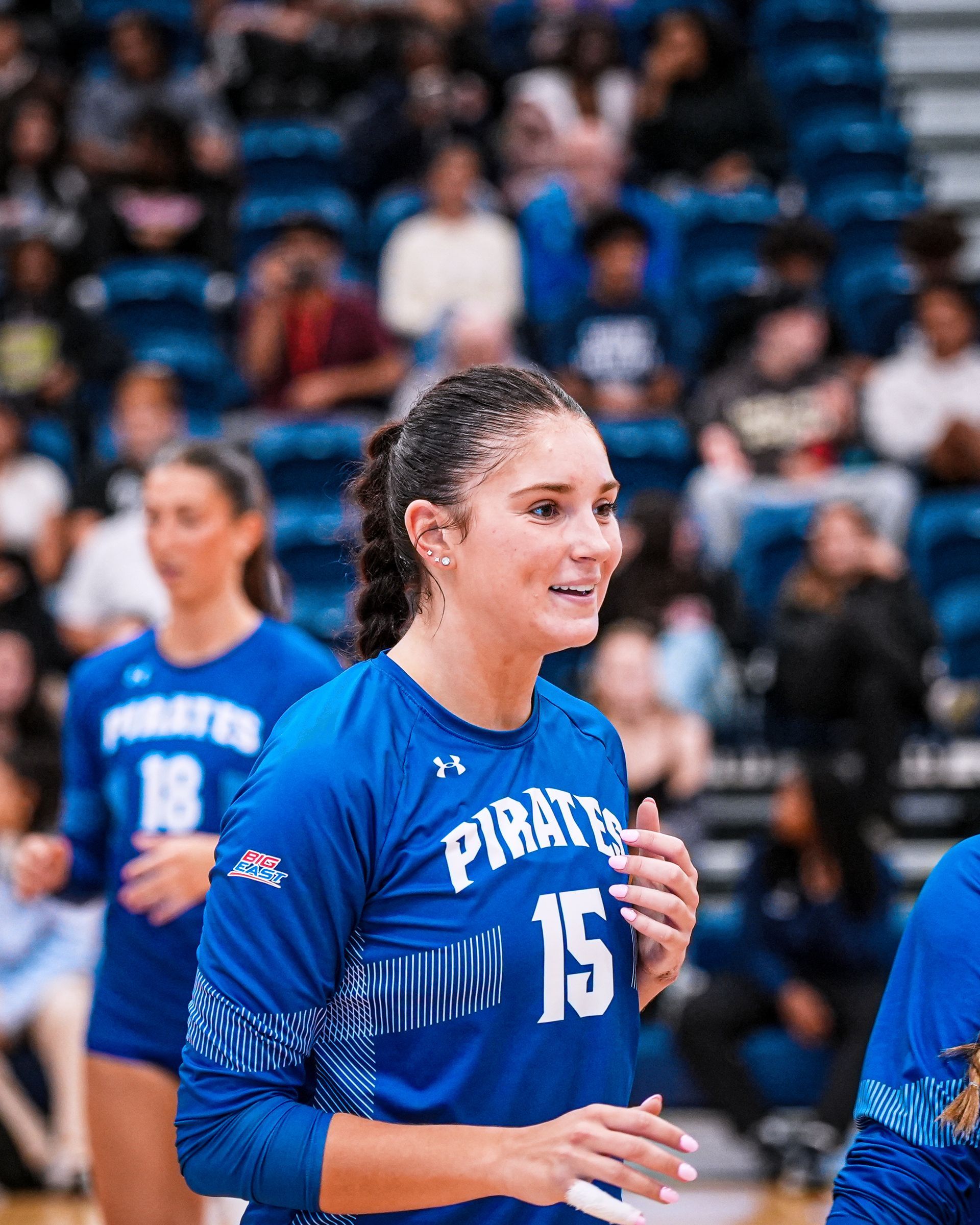 Volleyball player in blue Pirates jersey smiling on court during a game