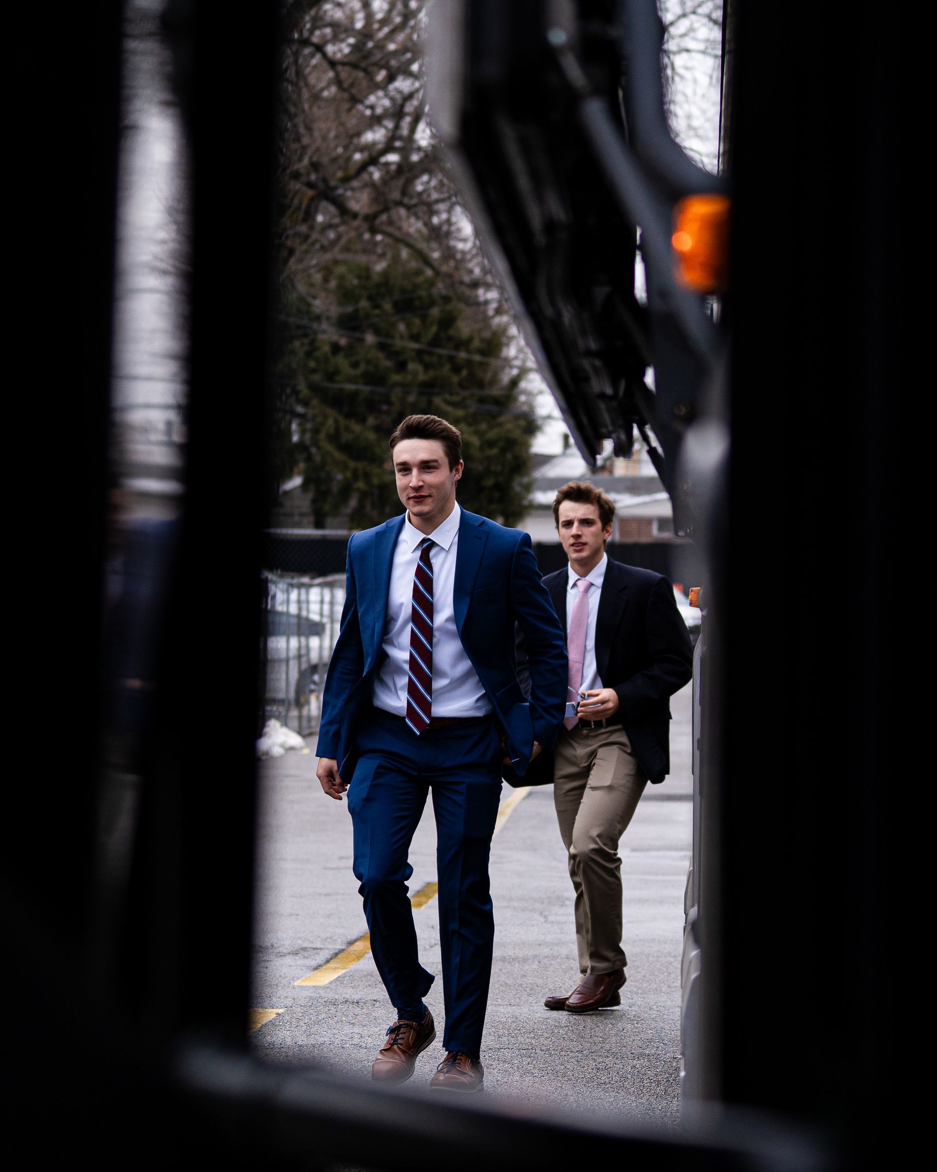Two men in suits walking outdoors on a gravel path near a building.
