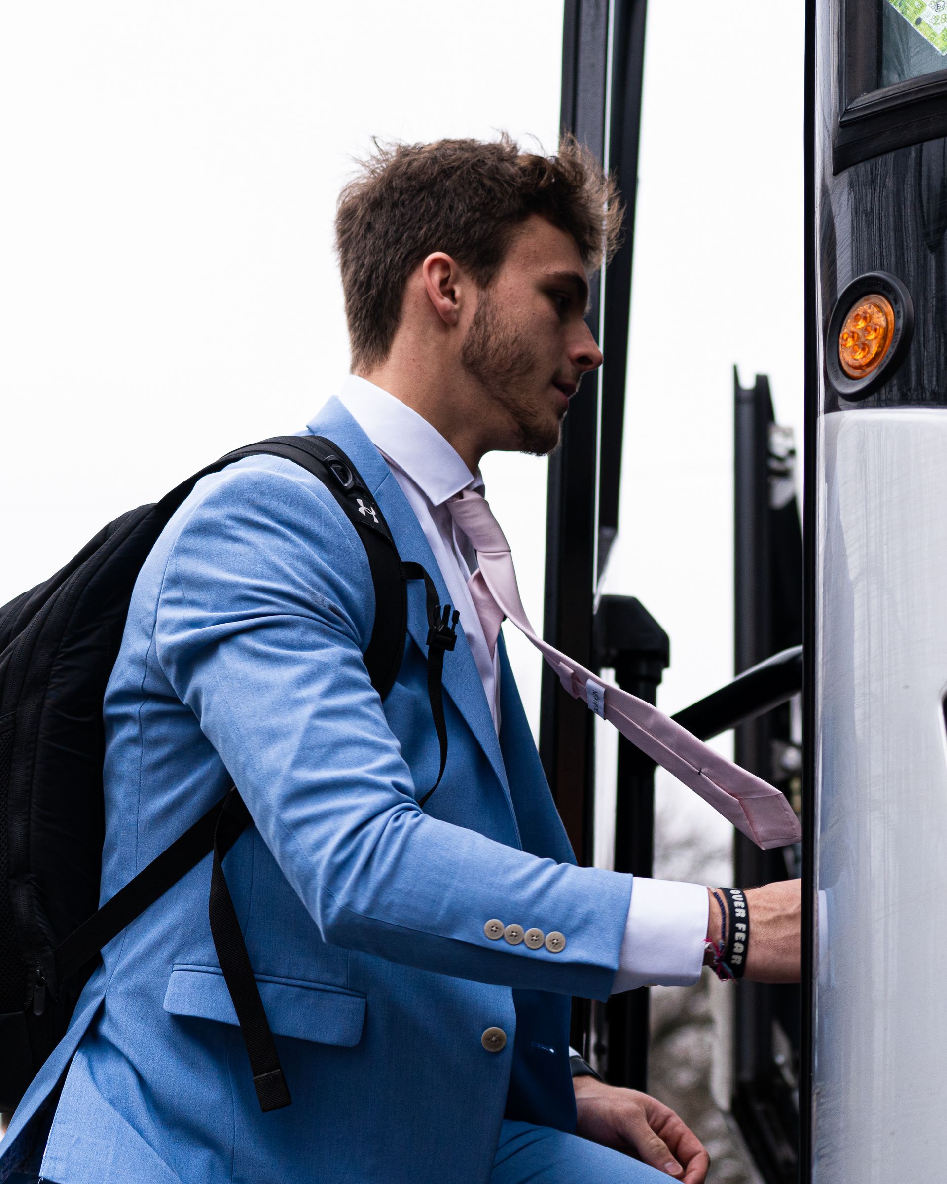 Man in blue blazer boarding a bus, holding the door handle and wearing a backpack