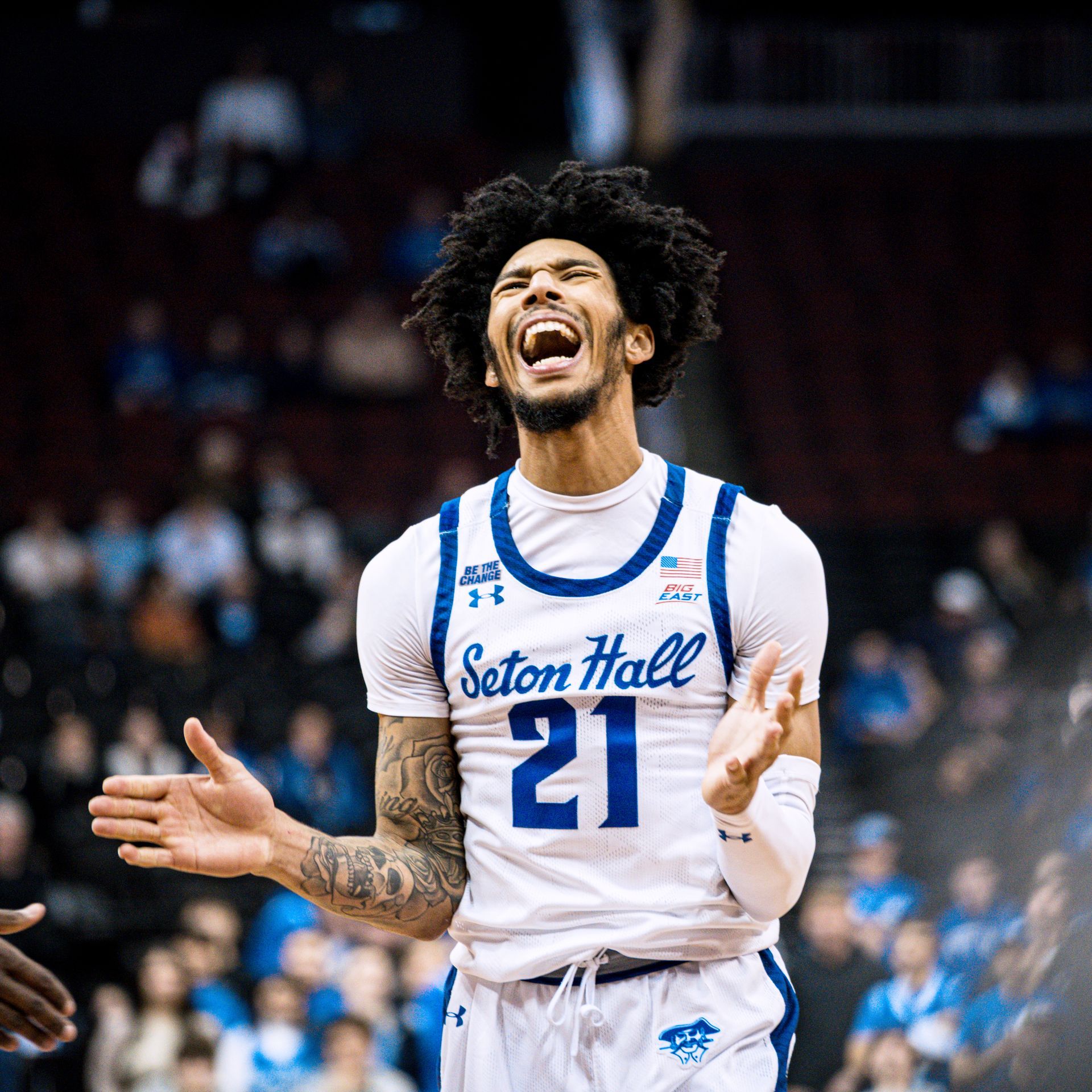 Basketball player in white Seton Hall jersey #21 cheering with arms outstretched on court