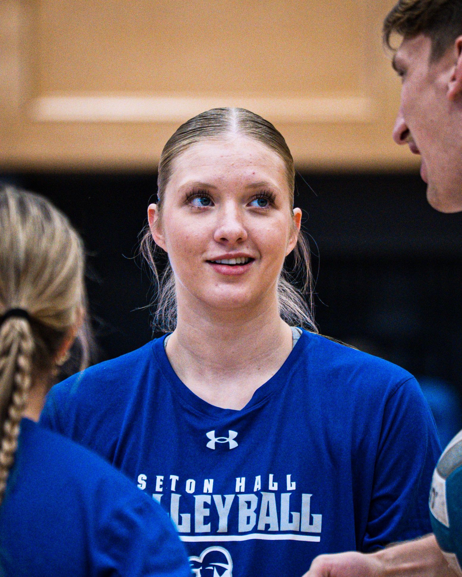 Volleyball player in blue Seton Hall jersey speaking with teammates in a gym
