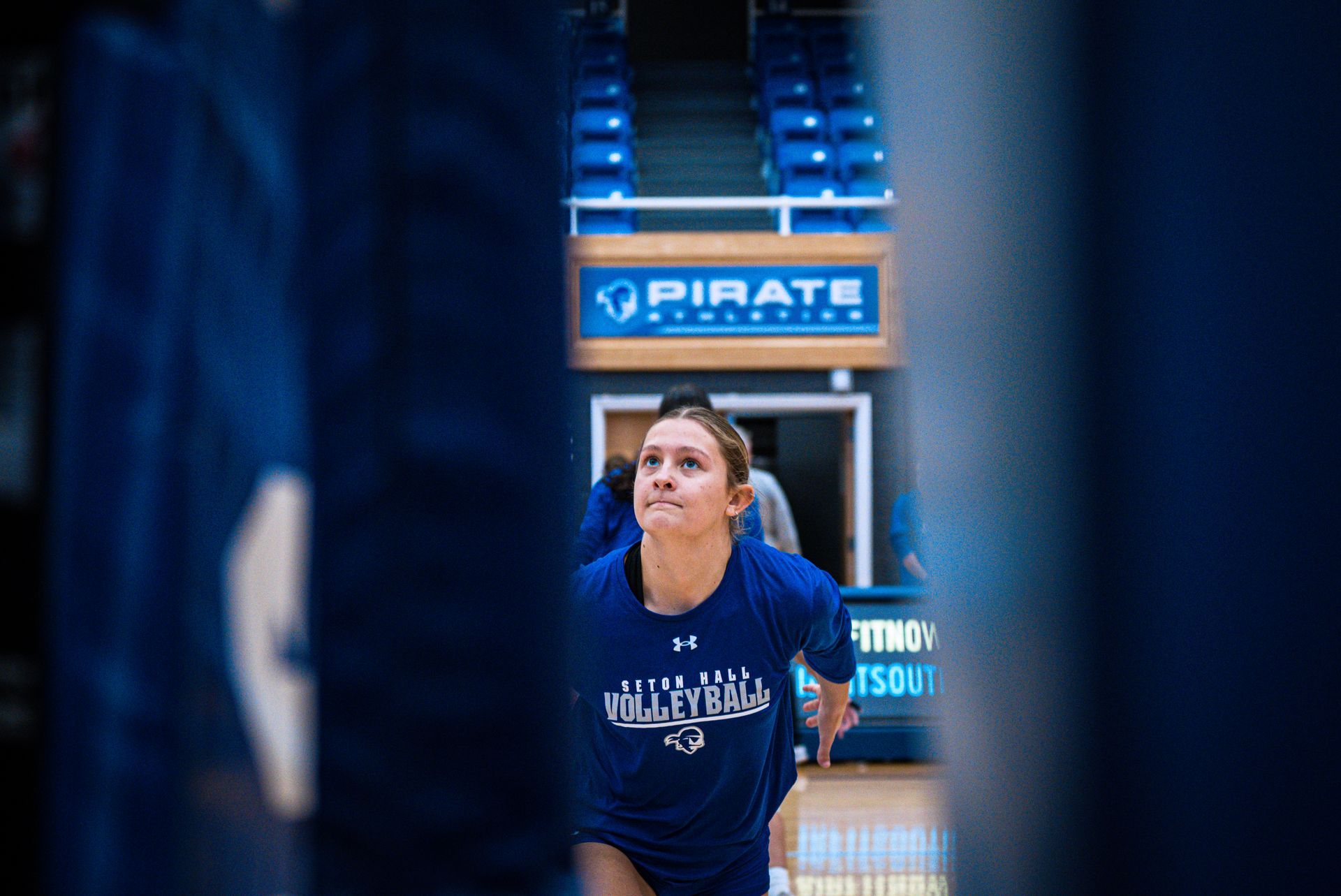 Basketball player in blue warm-up shirt on court, facing up toward the hoop.