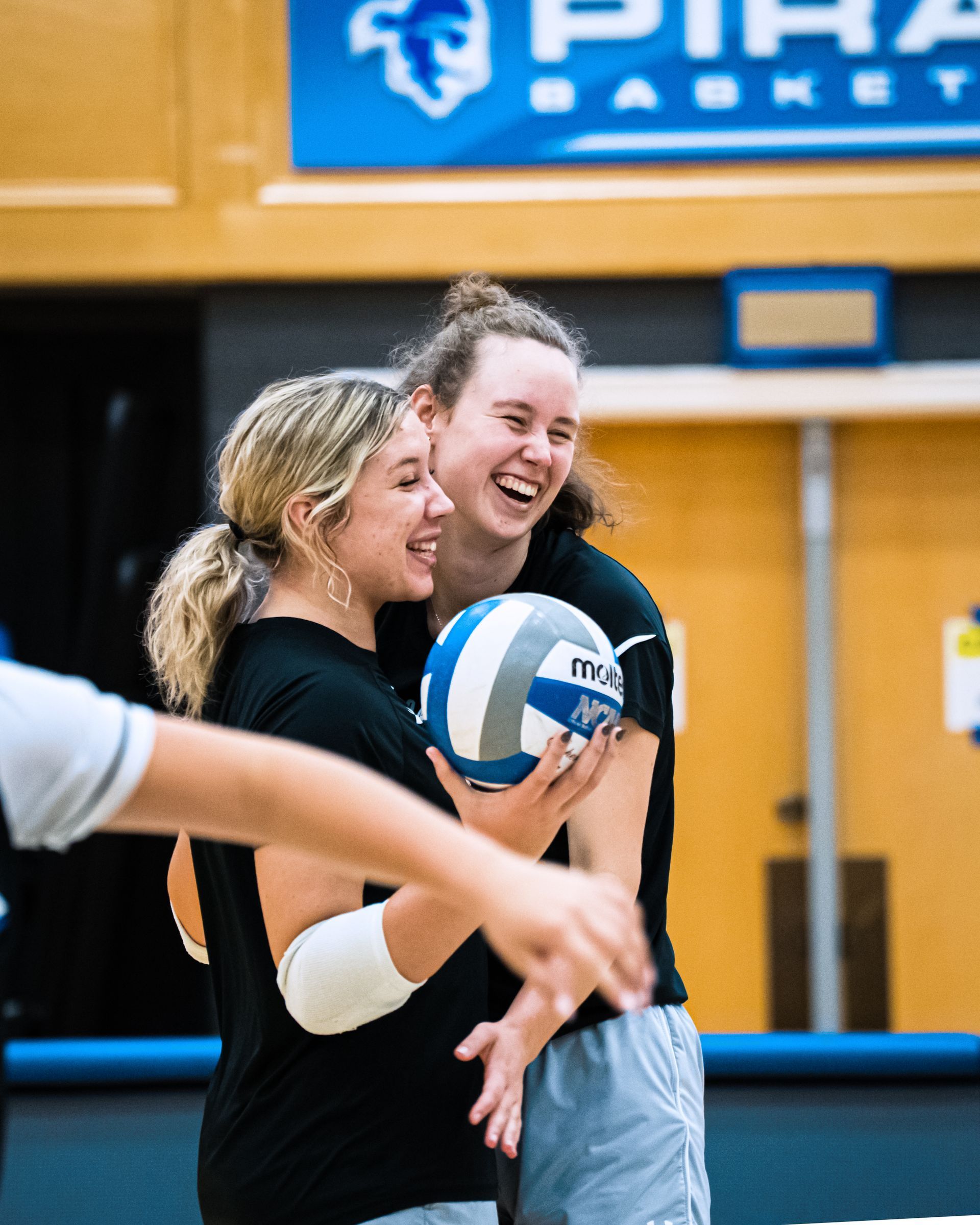Two volleyball players smiling and holding a ball in a gymnasium