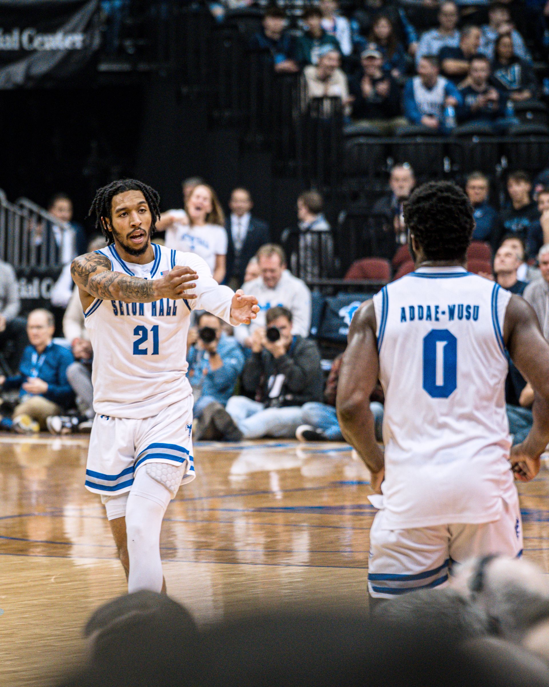 Basketball players in white jerseys on an indoor court, one pointing during play.