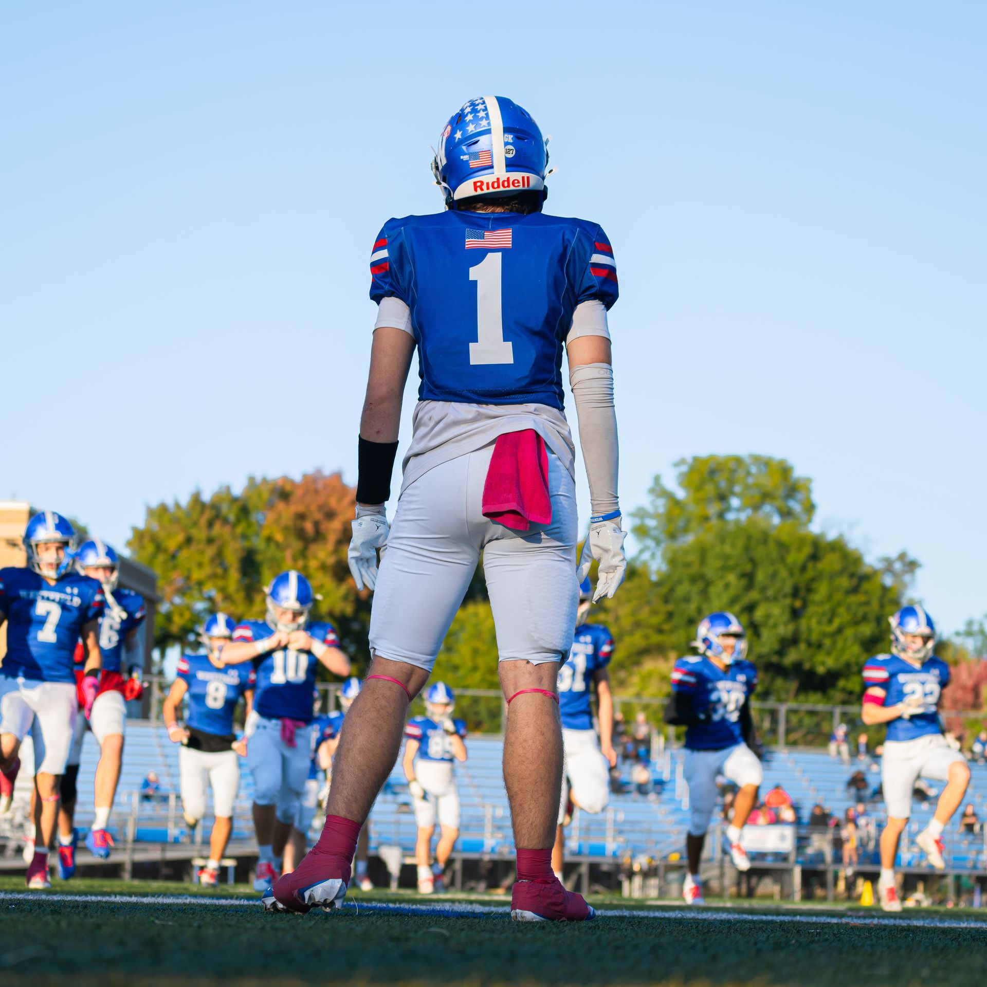 Football players in blue uniforms on a field, with player number 1 standing in the foreground.