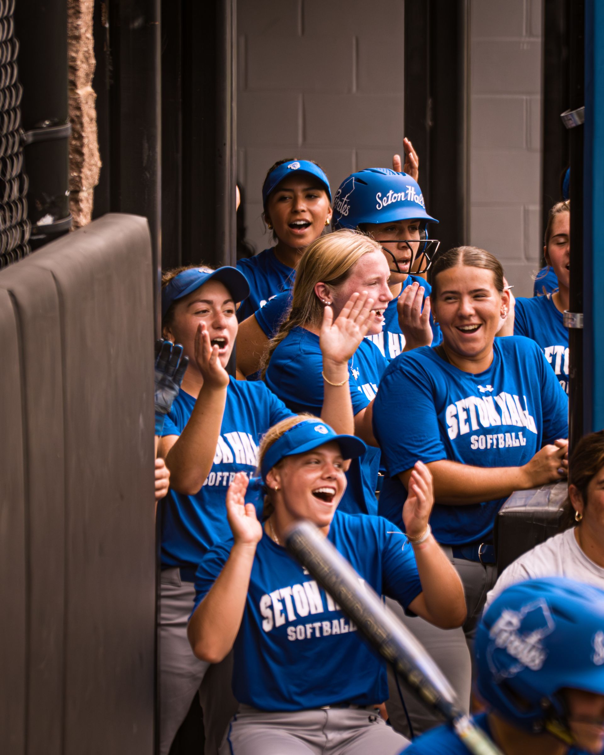 Blue-clad fans cheering and clapping in a stadium corridor, with helmets and smiles.
