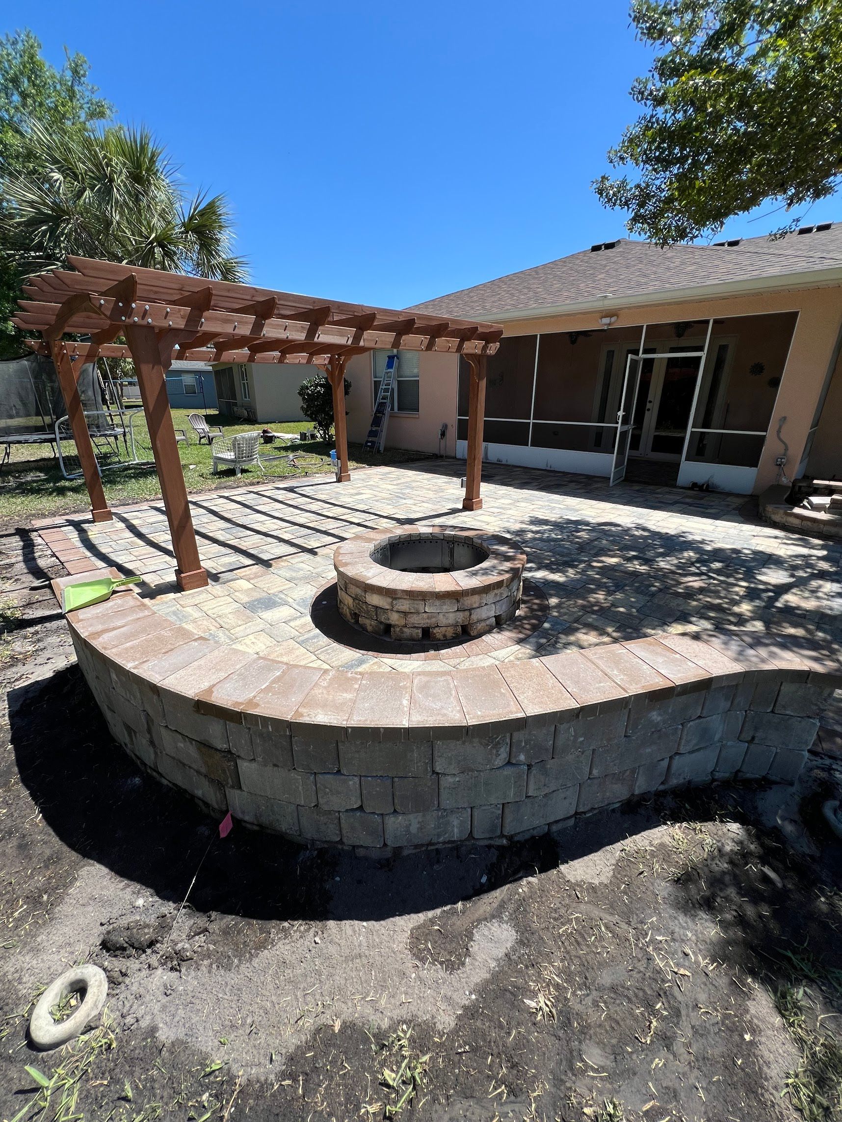 A fire pit is sitting under a pergola in front of a house.