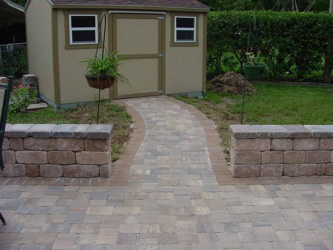 A brick walkway leading to a shed in a backyard.