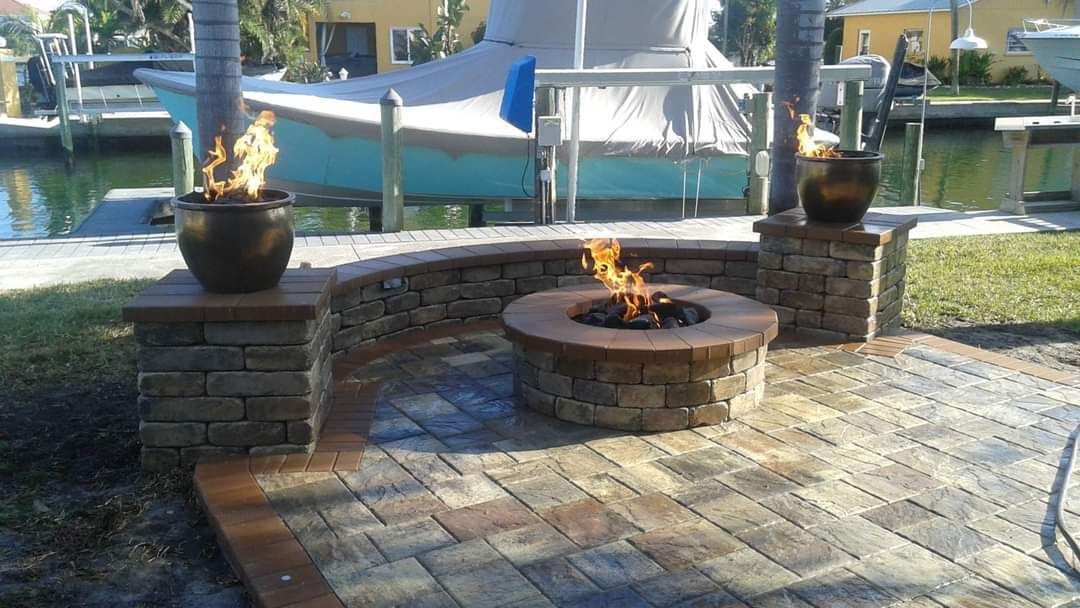 A fire pit is sitting on top of a brick patio next to a body of water.