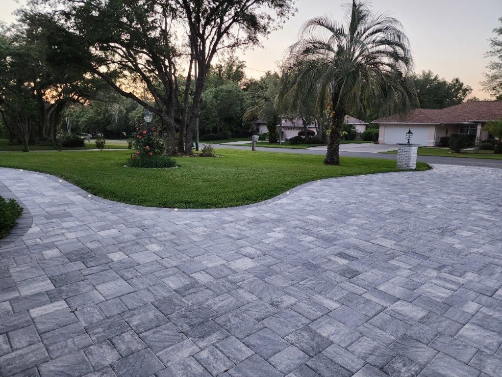 A brick driveway leading to a house with palm trees in the background