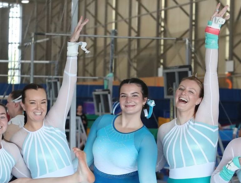 A group of gymnasts are posing for a picture in a gym with their coaches.