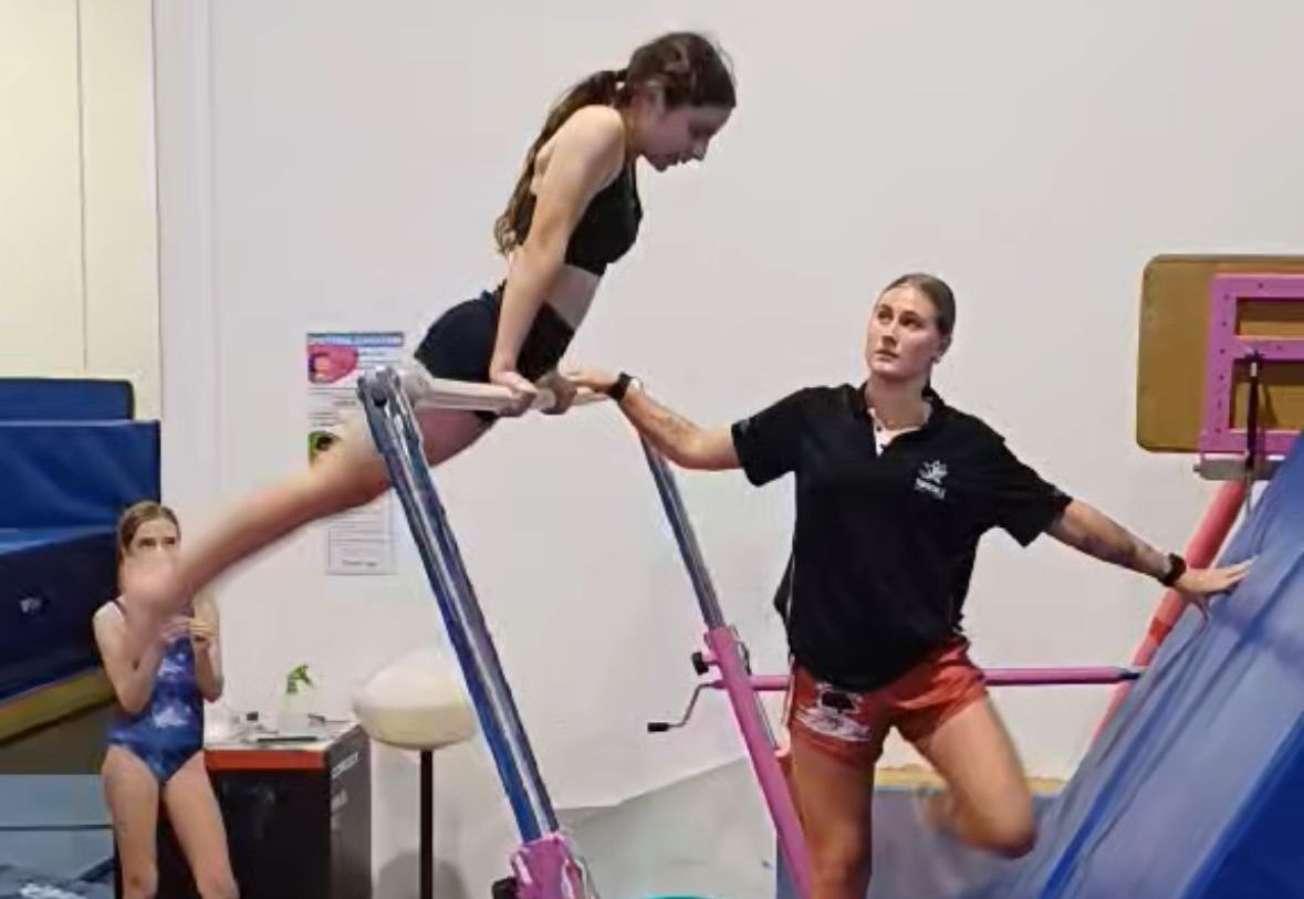A coach is helping a young girl on uneven bars.