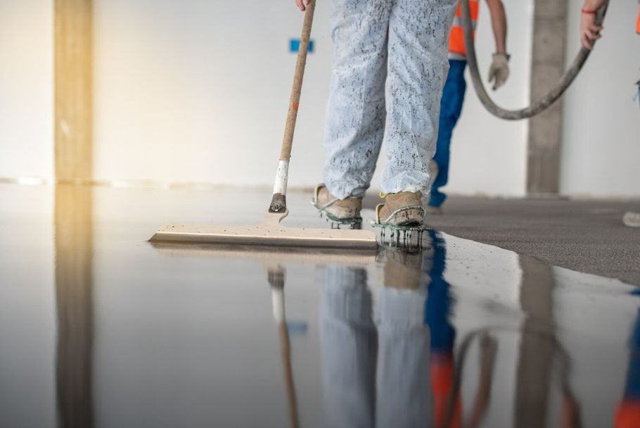 Worker smoothing a glossy concrete floor with a long-handled tool in a bright room