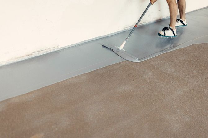 Person smoothing wet gray concrete floor with a trowel indoors
