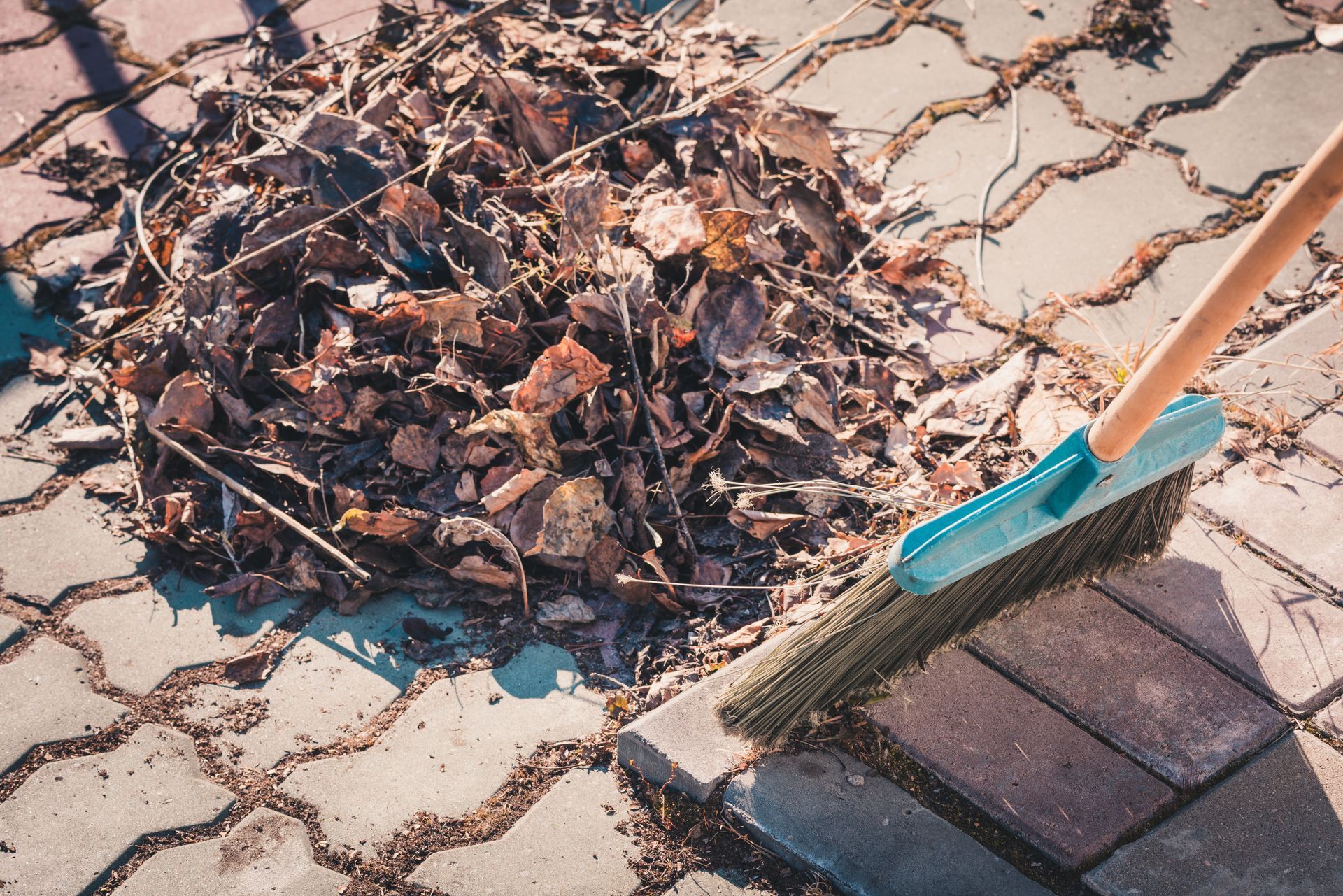 Broom sweeping dried leaves on a brick paved surface.