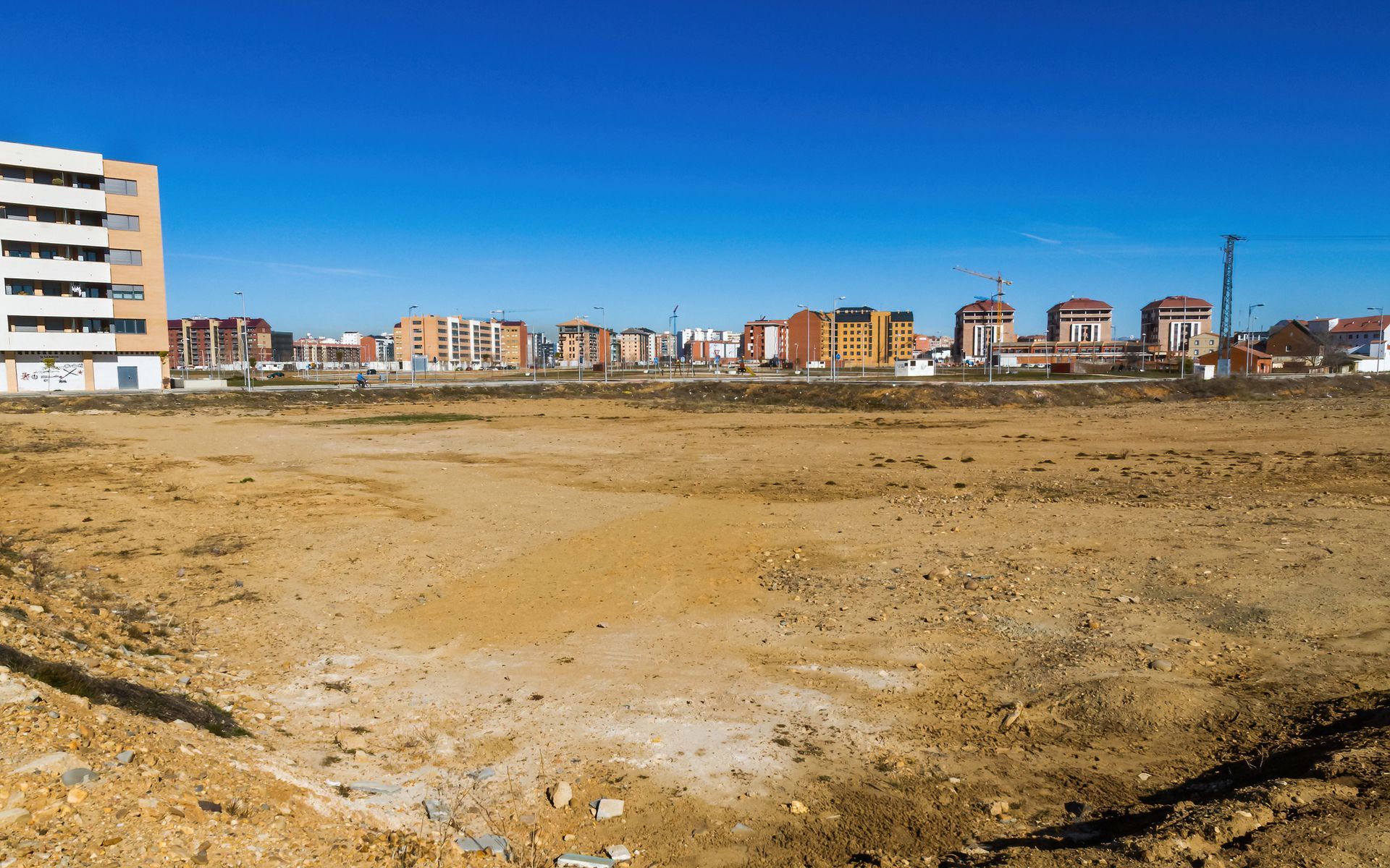 Brown, empty lot in front of various apartment buildings under a clear, blue sky.