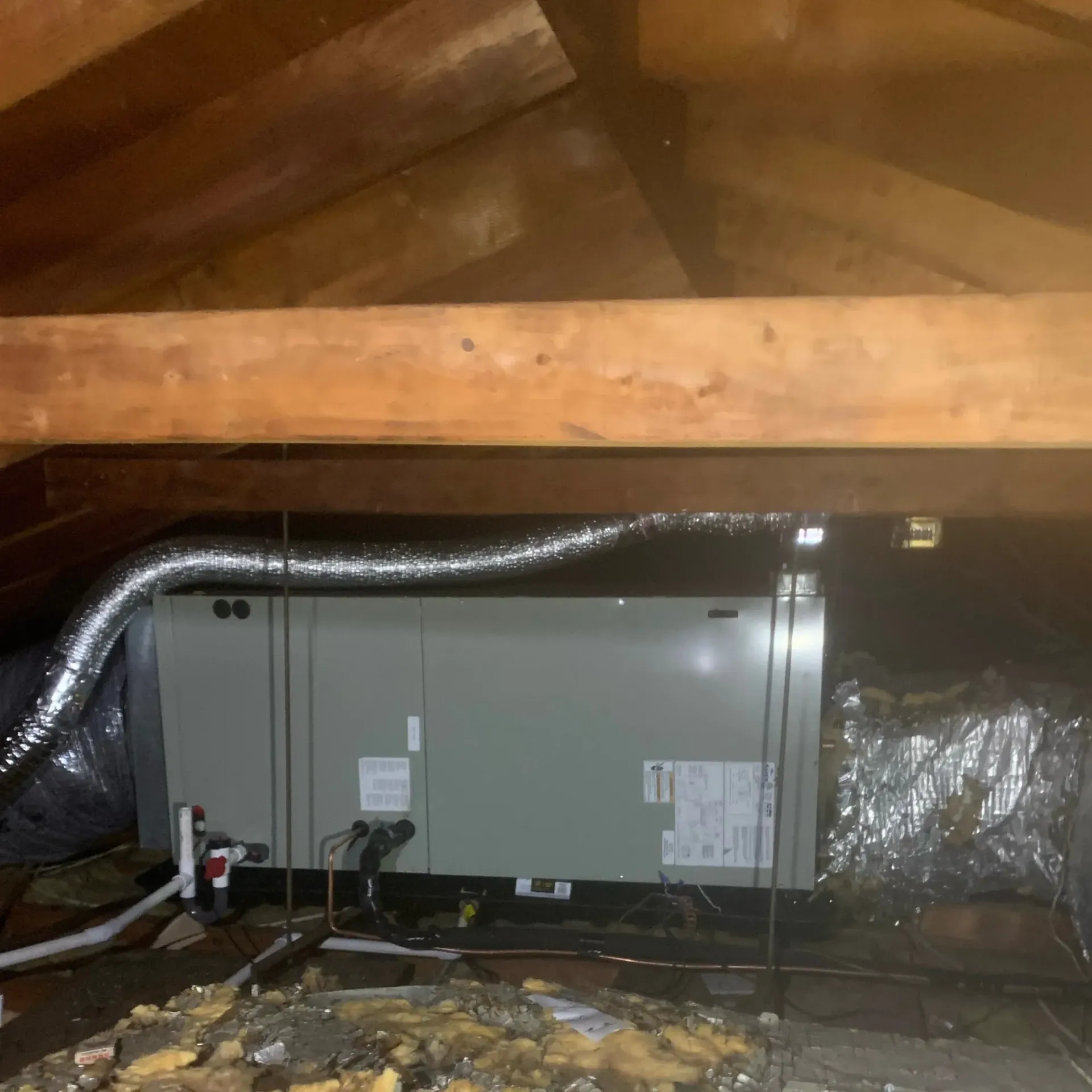 Apex Climate Control - An air conditioner is being installed in an attic under a wooden ceiling.