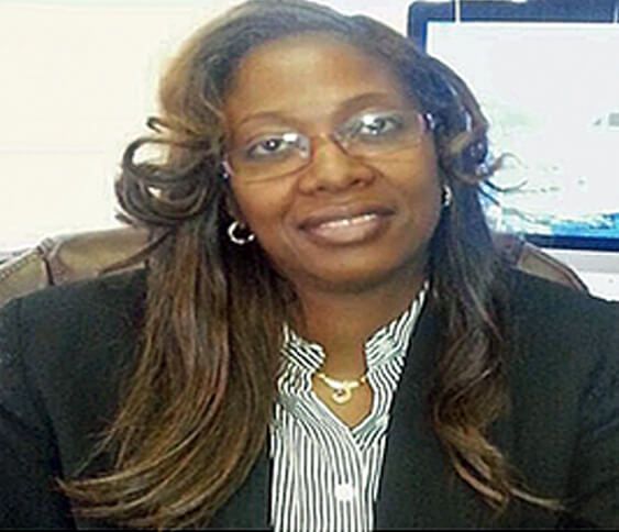 A woman wearing glasses and a black jacket is sitting in front of a computer.