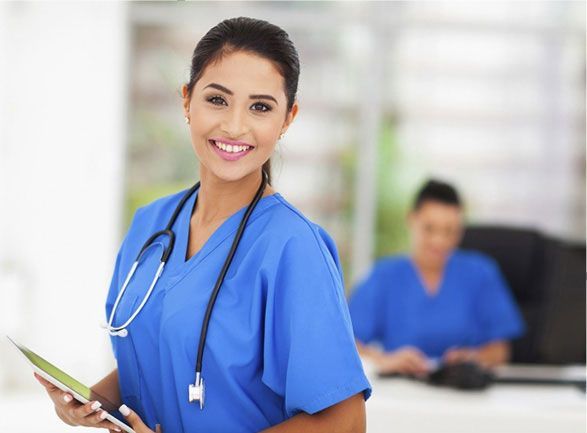 A nurse with a stethoscope around her neck is holding a tablet and smiling.