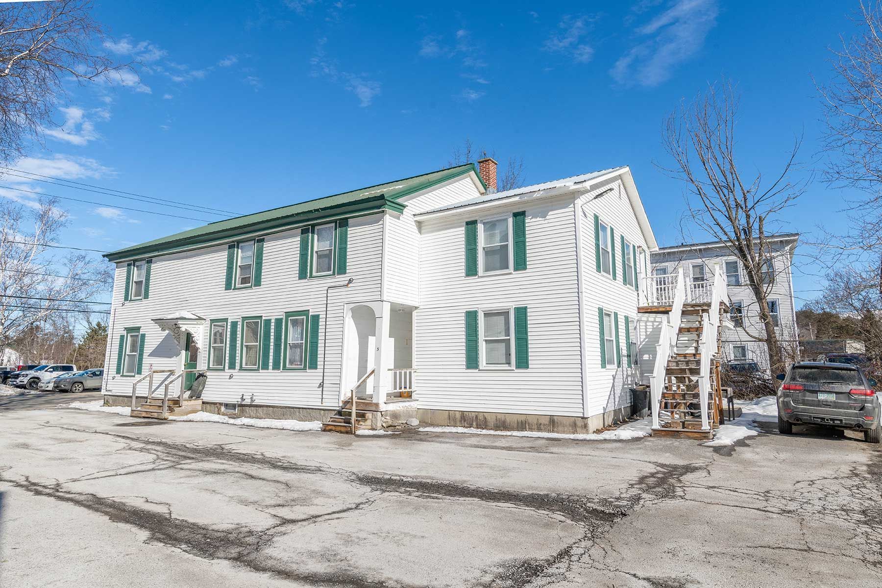 Snow-covered white building at Elm Complex with green-trimmed windows and exterior staircase under blue sky.