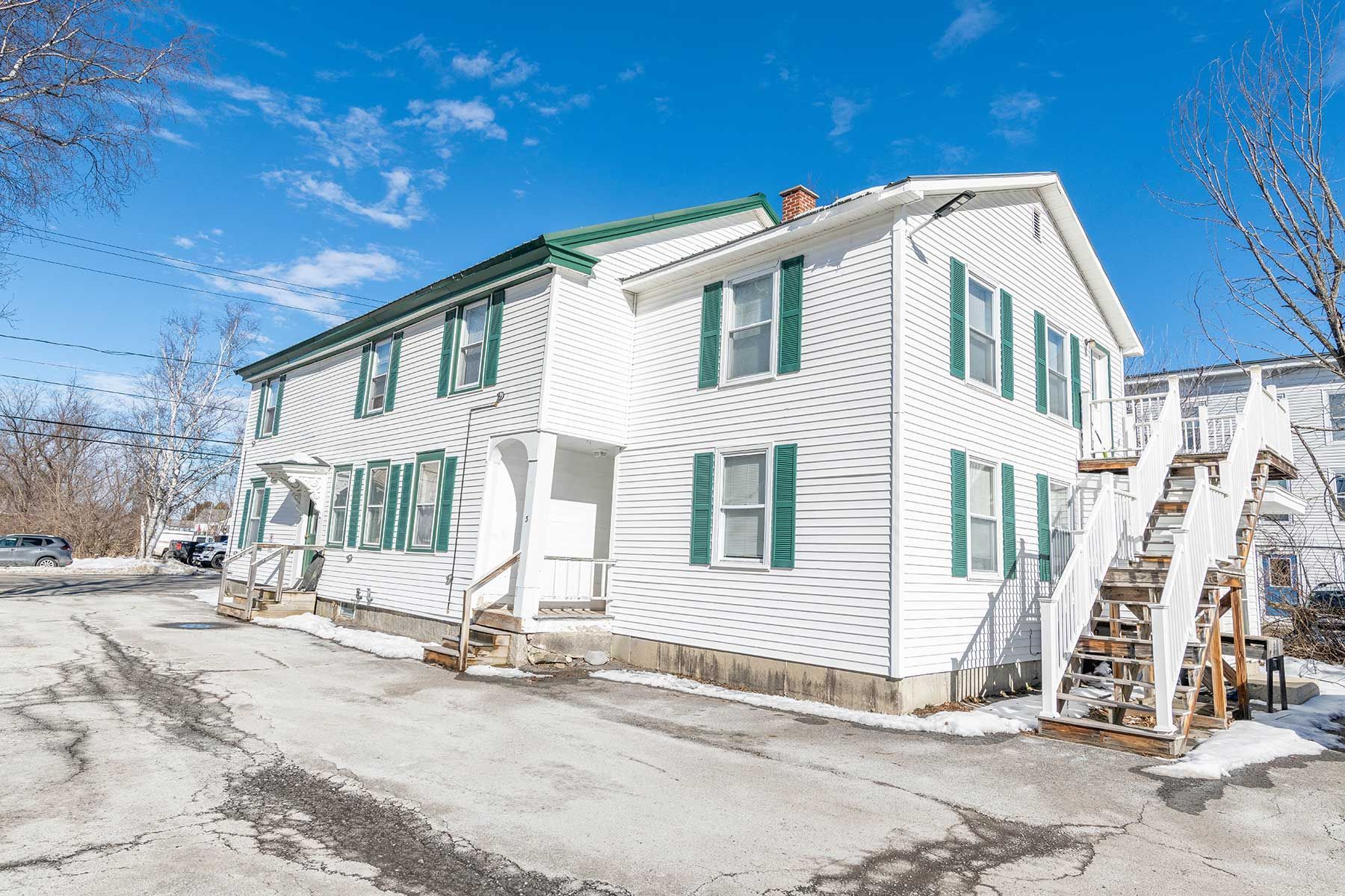 Snow-covered white house with green shutters under a bright blue sky at Elm Complex in New Hampshire.