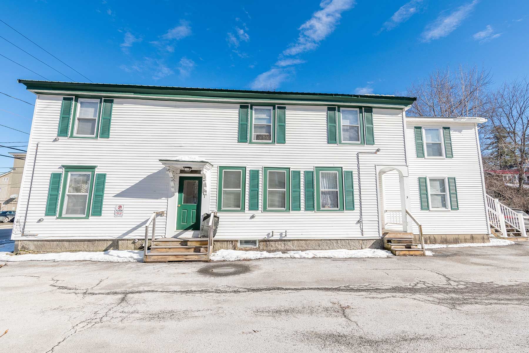 White two-story house with green trim and shutters in a snowy street scene at Elm Complex in New Hampshire.