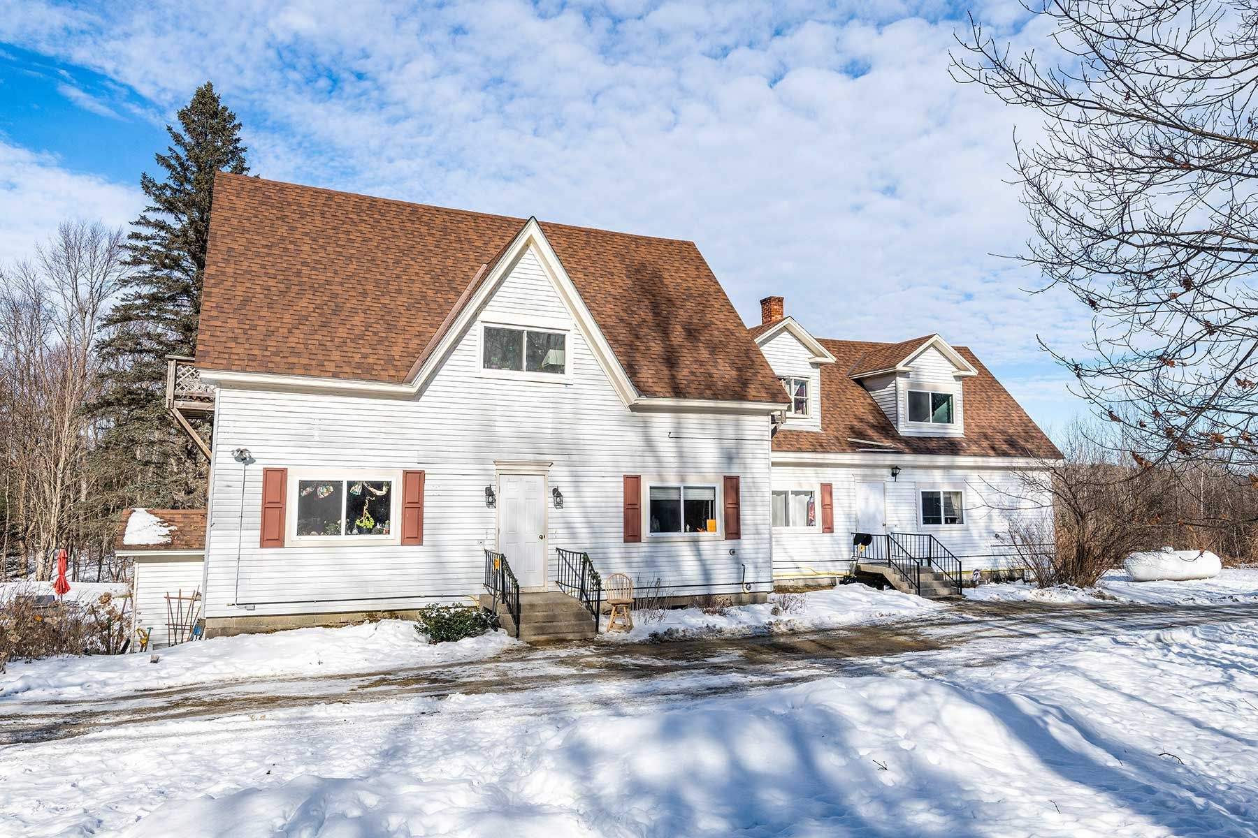 Snow-covered suburban house with white siding and brown roof at Bickford Hill Complex on a sunny winter day.