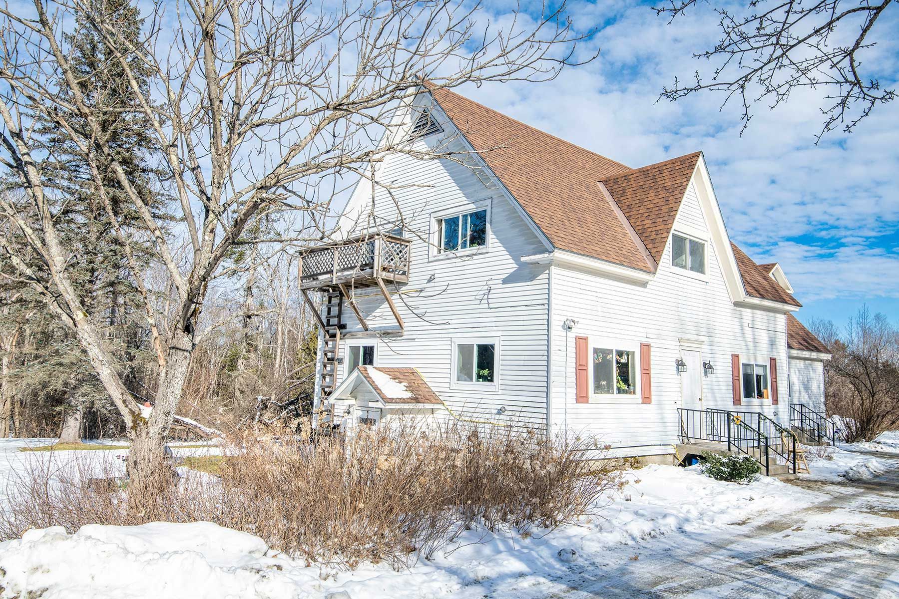 White house with red roof at Bickford Hill Complex  NH in a snowy yard beside bare trees on a bright winter day.
