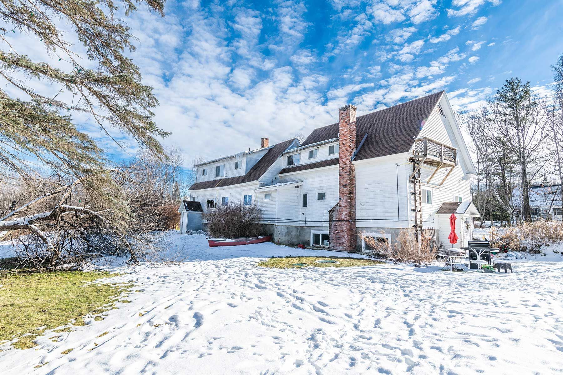Snow-covered white house with red brick chimney under a bright blue winter sky at Bickford Hill Complex.