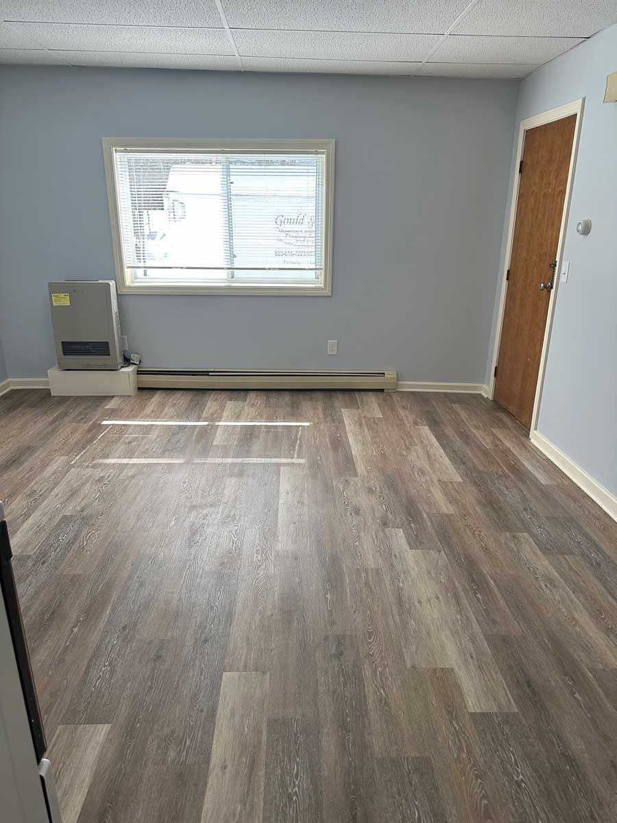Empty room at Bickford Hill Complex  NH with gray walls, wood-look flooring, window, and two doors.
