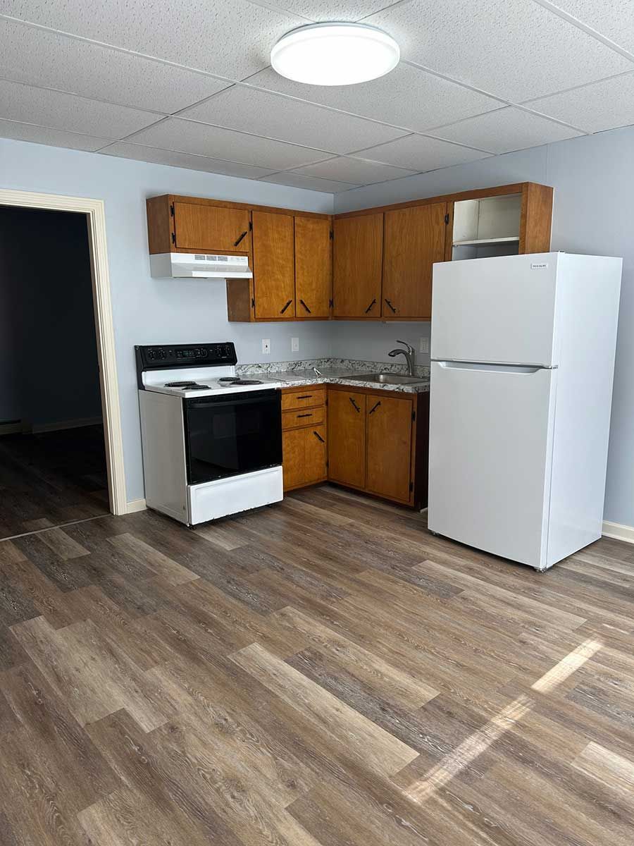 Kitchen at Bickford Hill Complex NH with white appliances, wood cabinets, and wood flooring.