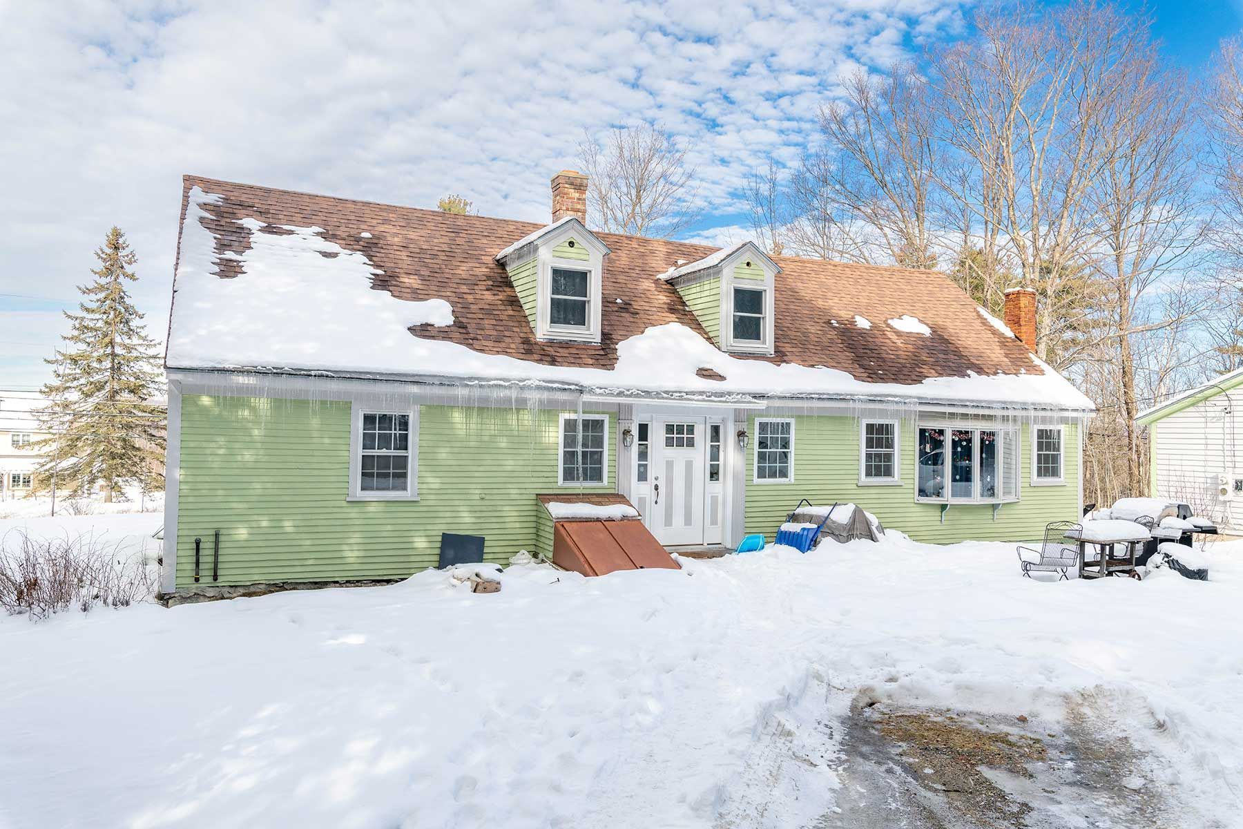 Snow-covered pale green house with dormer windows and red roof in a bright winter landscape