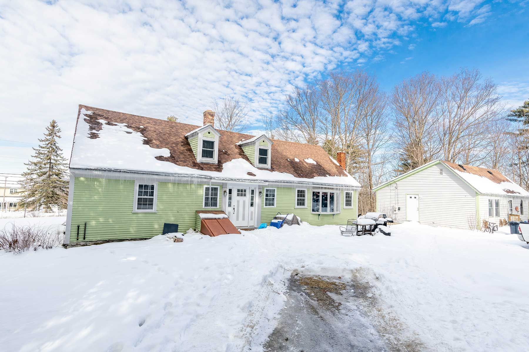 Snow-covered green house with detached garage on a bright winter day