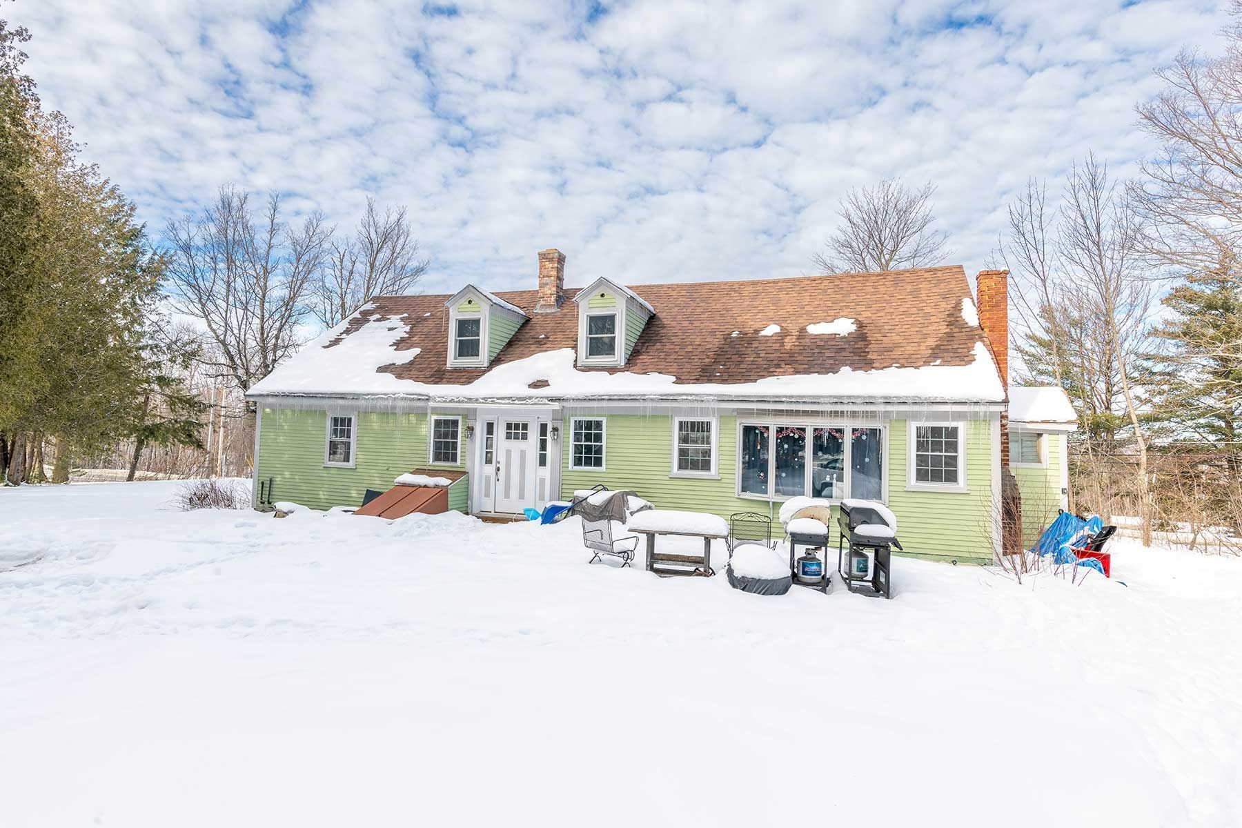 Snow-covered green house with red roof and outdoor chairs in a snowy winter yard